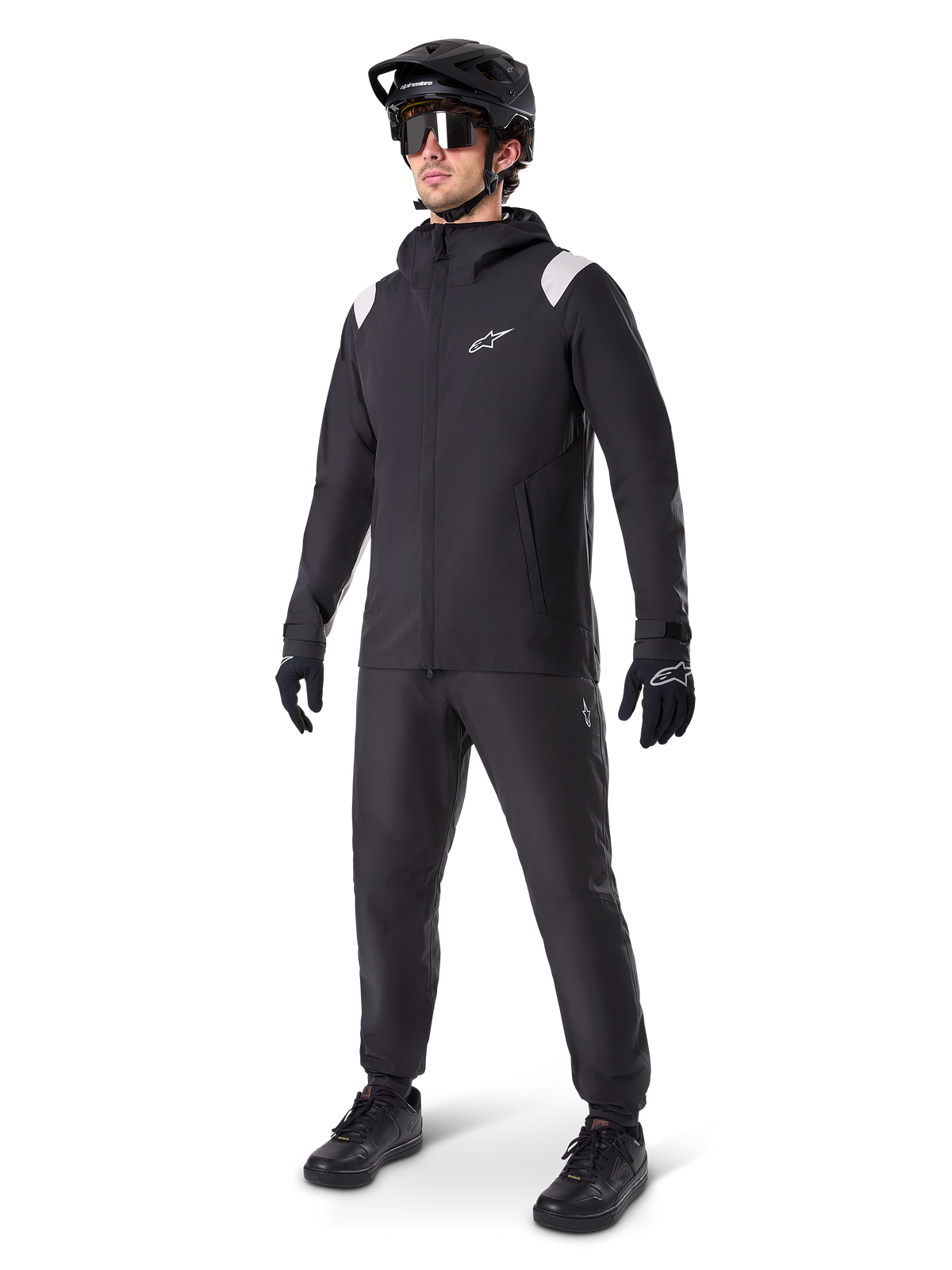 Casaco Alpinestars A-Dura Rain, casaco de chuva preto para BTT, com detalhes brancos nos ombros, usado por um ciclista com capacete de BTT preto, óculos de sol, luvas e calças a condizer, conjunto técnico de ciclismo para todas as condições climatéricas