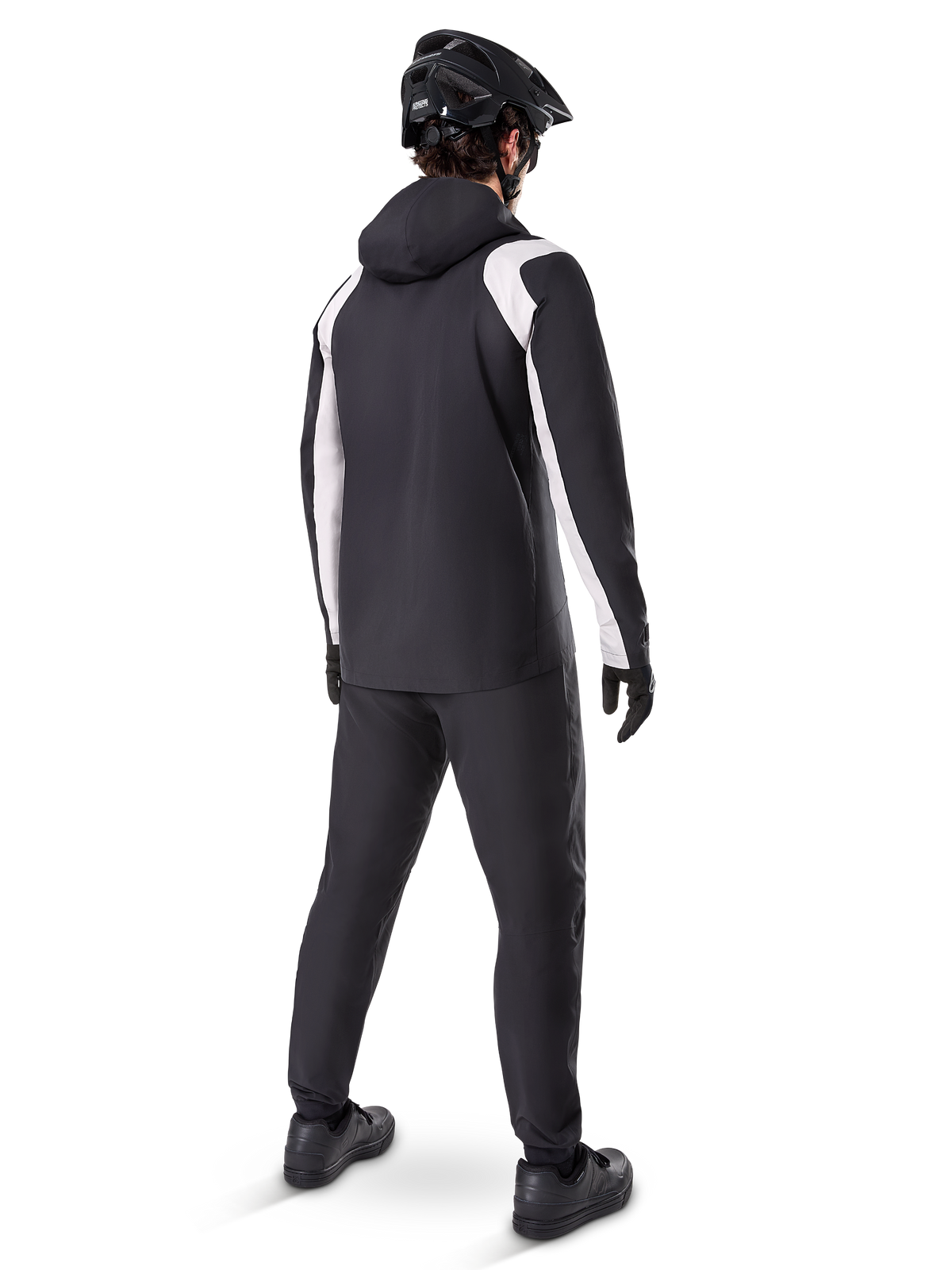 Alpinestars A-Dura Rain Jacket, vista traseira de um ciclista masculino a usar o casaco de BTT impermeável preto e branco, calças de ciclismo pretas a condizer, capacete preto e luvas, equipamento técnico para BTT em condições de chuva.