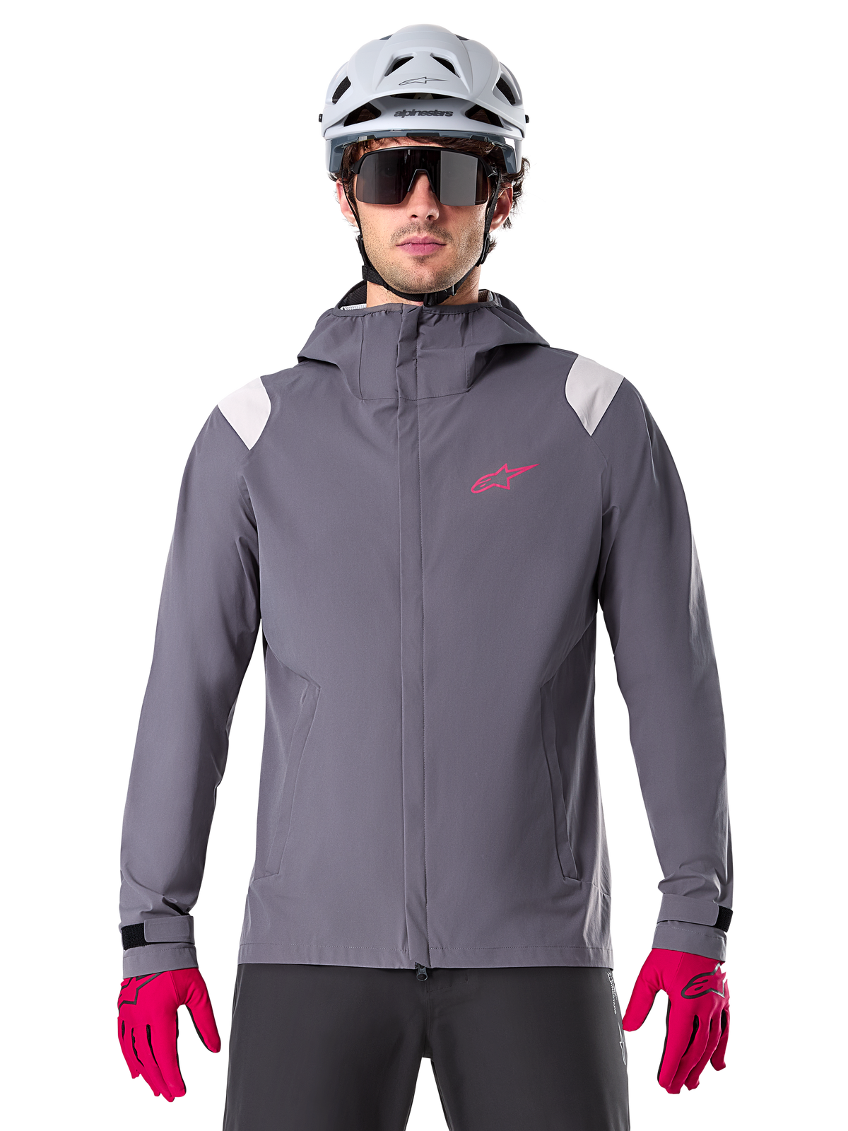 Alpinestars A-Dura Rain Jacket, casaco de chuva para BTT, cinzento Dark Titanium, design com capuz com logótipo Alpinestars cor-de-rosa e painéis nos ombros em cinzento claro, usado com capacete de BTT branco e luvas cor-de-rosa vibrante, equipamento impermeável para ciclismo todo-o-terreno