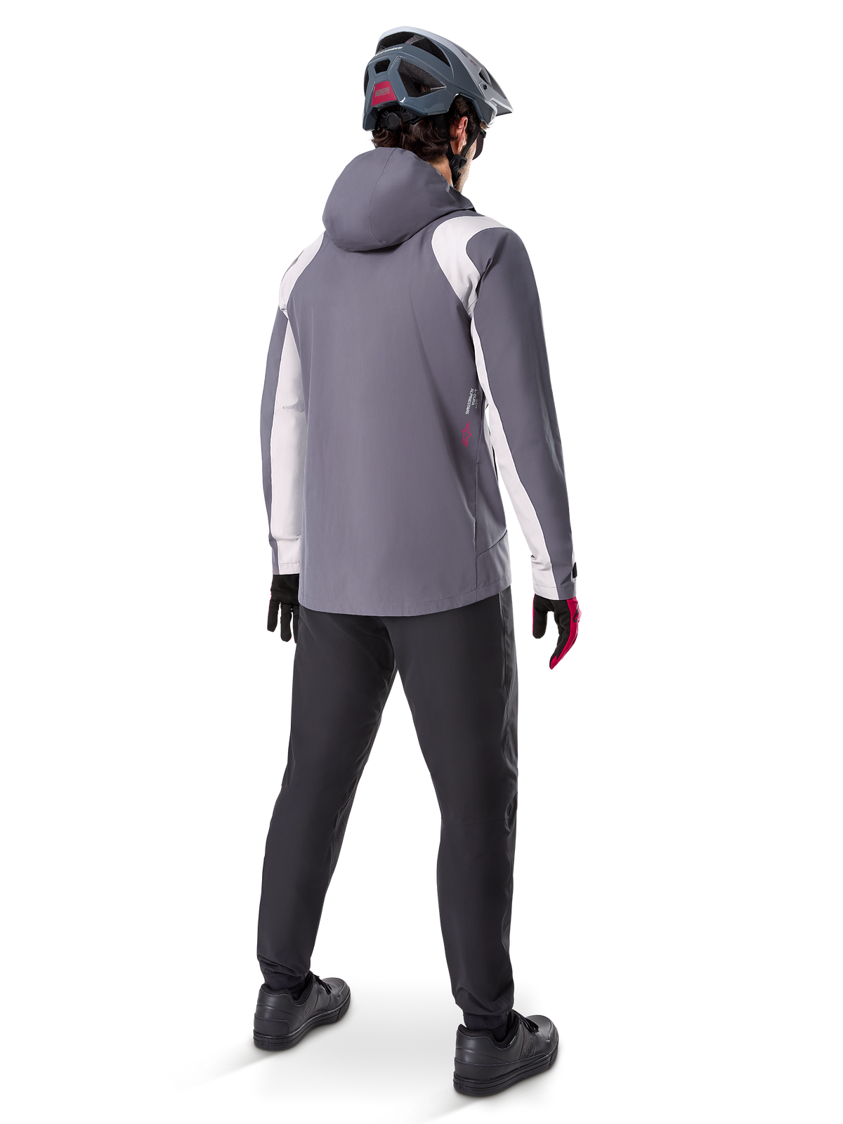 Alpinestars A-Dura Rain Jacket, casaco de BTT, cinzento Dark Titanium com painéis brancos, vista traseira de ciclista com capacete cinzento e calças pretas, equipamento técnico para tempo chuvoso
