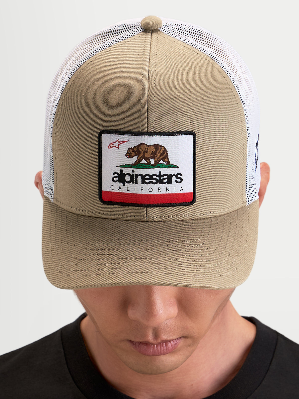 Alpinestars Chapéu Cali 2.0, boné trucker sportswear, castanho e branco, com coroa estruturada em sarja, patch do urso da Califórnia e parte traseira em malha respirável, visto num modelo