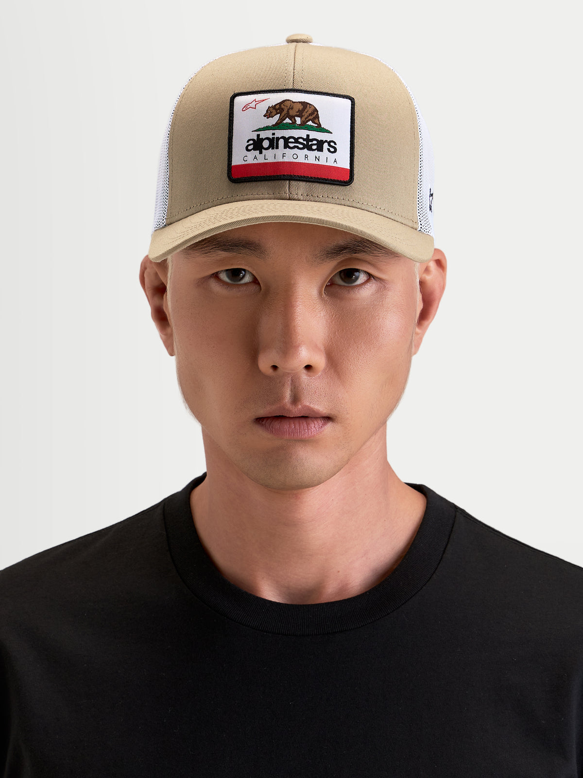 Alpinestars Chapéu Cali 2.0, boné trucker sportswear, caqui e branco, com aba curva, coroa estruturada em sarja, malha respirável traseira e remendo frontal do urso da Califórnia, usado por um modelo