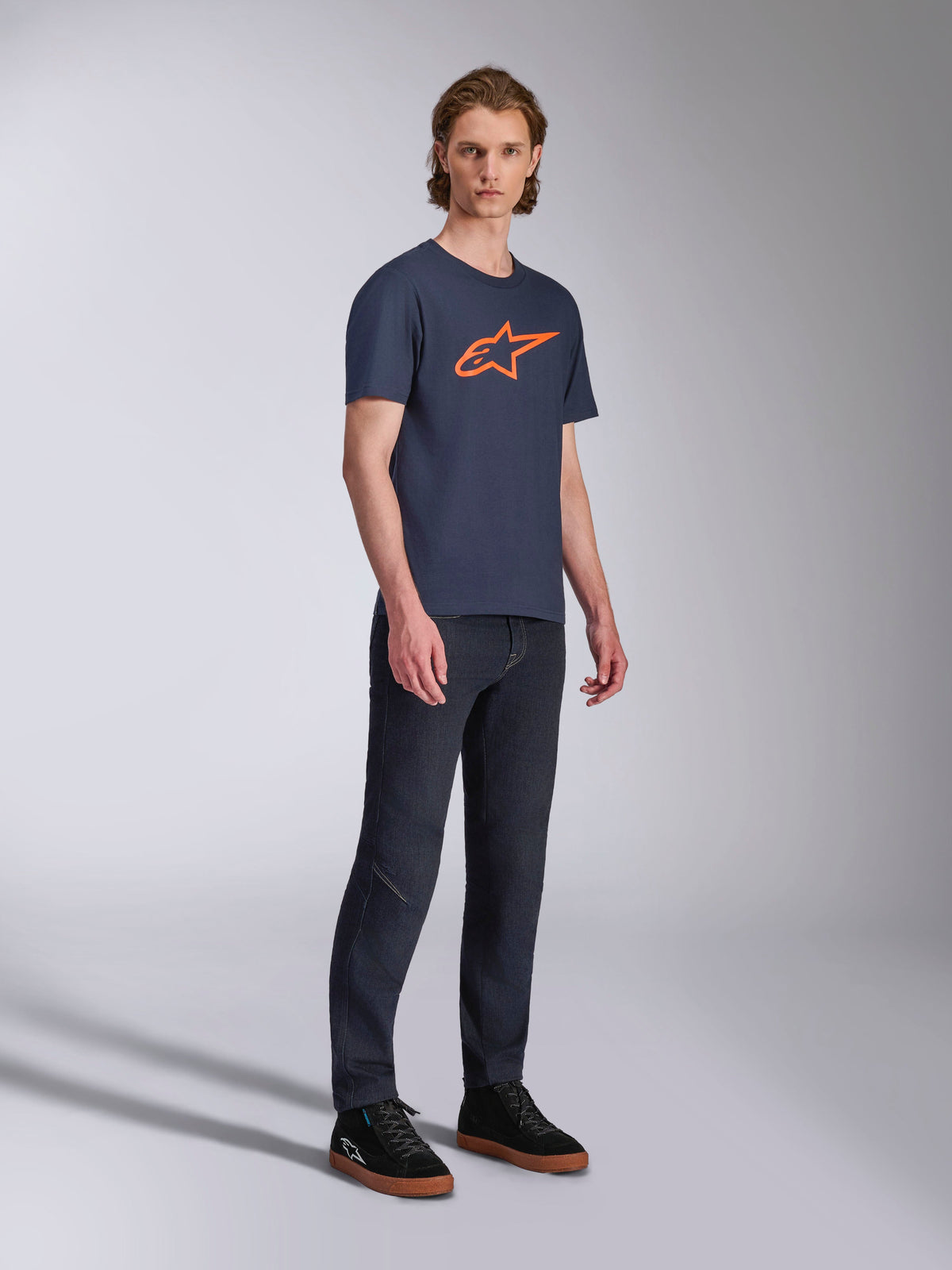 Alpinestars Ageless 2.0 CSF Tee, T-shirt de manga curta, azul-marinho com logótipo de estrela laranja, usada com calças de ganga escuras e sapatilhas pretas, streetwear casual inspirado no desporto motorizado