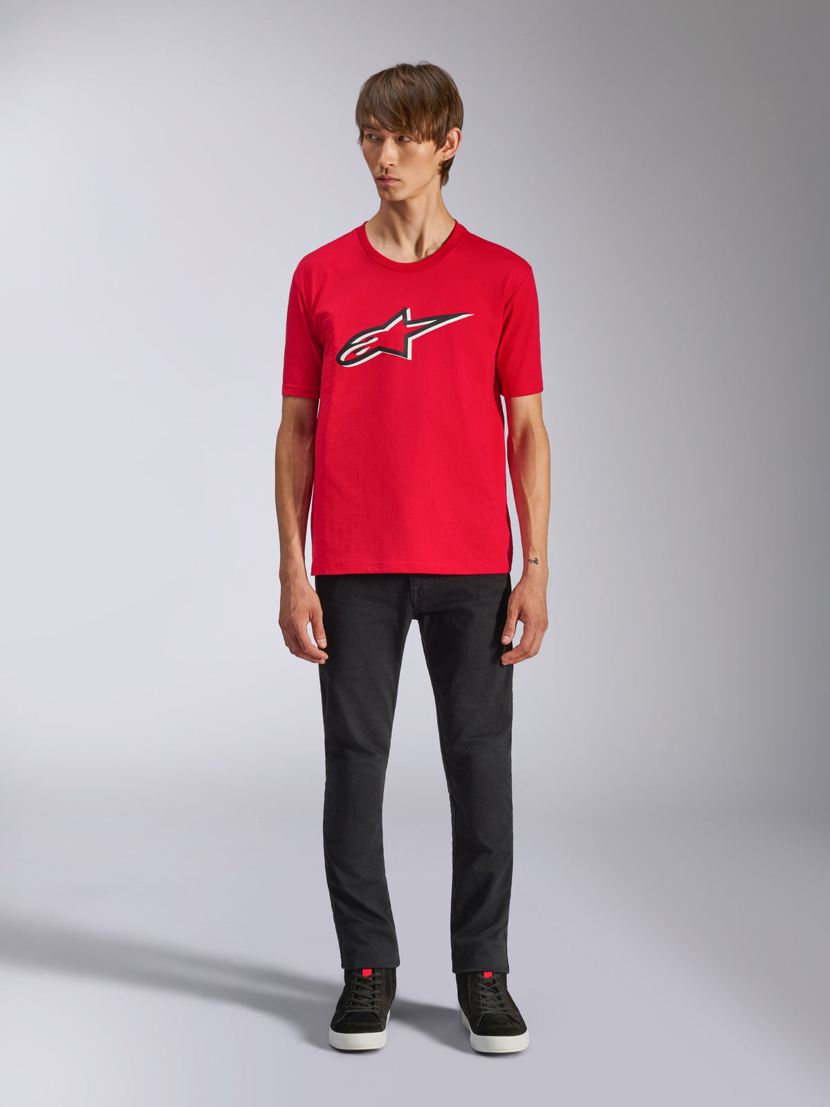 Alpinestars Ageless Shadow CSF Tee, t-shirt de manga curta, vermelha, logótipo Ageless frontal com contornos a branco e preto, vestida por um modelo com calças pretas e ténis, streetwear casual de motorsport