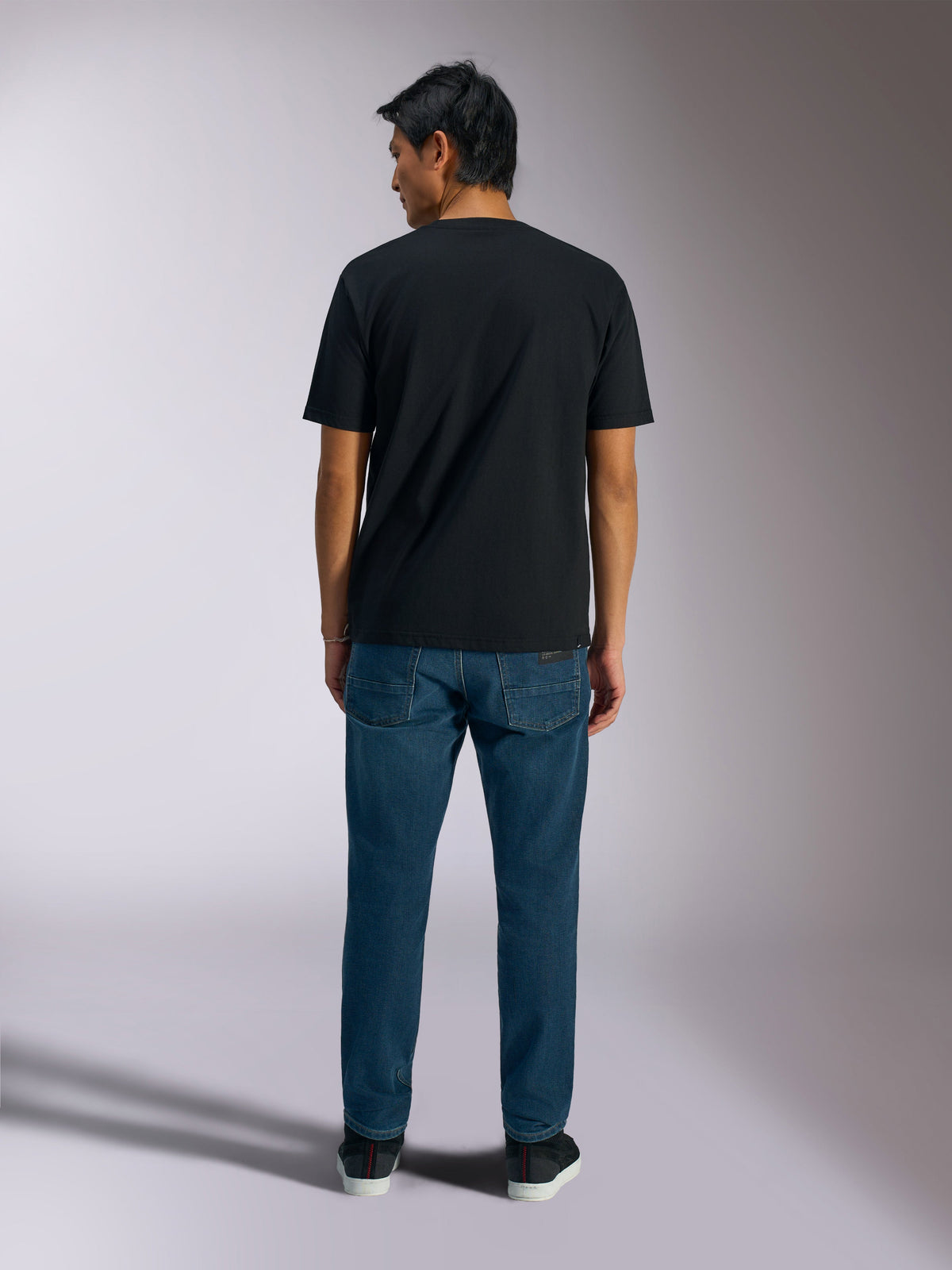 Alpinestars Ageless Shadow CSF Tee, t-shirt de manga curta, preta, vista traseira, usada com calças de ganga azuis, streetwear casual de desportos motorizados