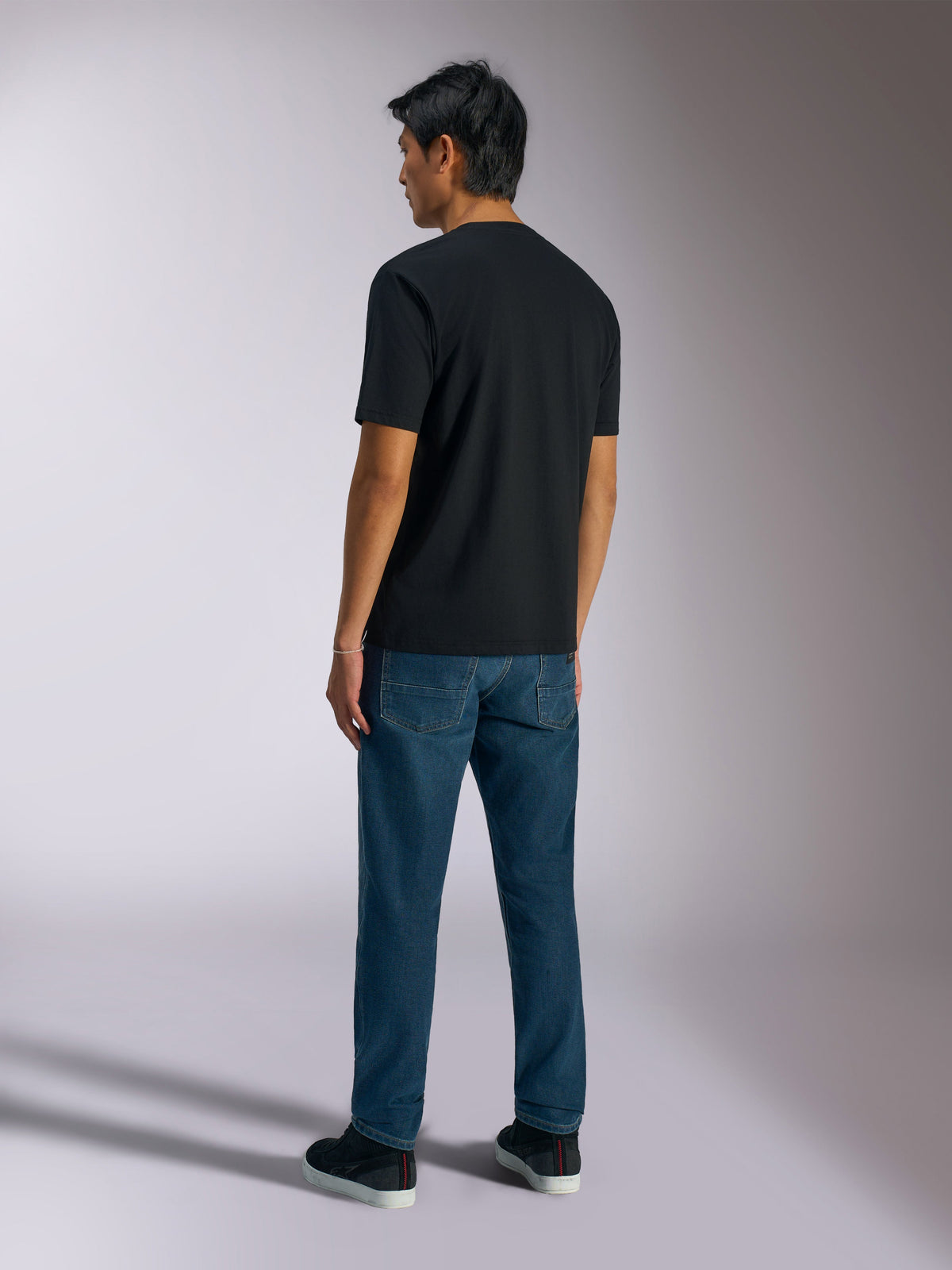 T-shirt Alpinestars Ageless Shadow CSF, t-shirt de manga curta, preta, vista traseira, usada com calças de ganga azuis e sapatilhas pretas, streetwear casual inspirado no desporto motorizado