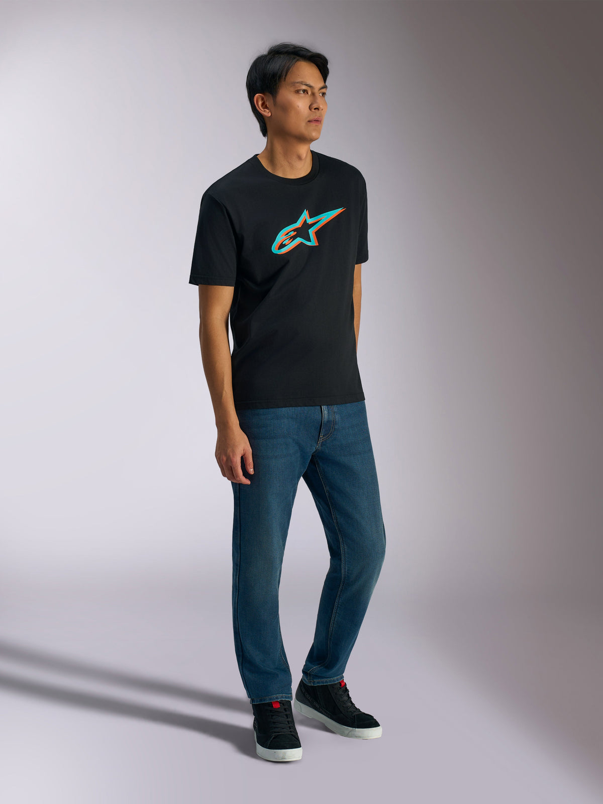 Alpinestars Ageless Shadow CSF Tee, t-shirt de manga curta, preta com logótipo em sombra turquesa e laranja, vestida por modelo masculino com calças de ganga azuis e sapatilhas pretas, streetwear casual inspirado no desporto motorizado