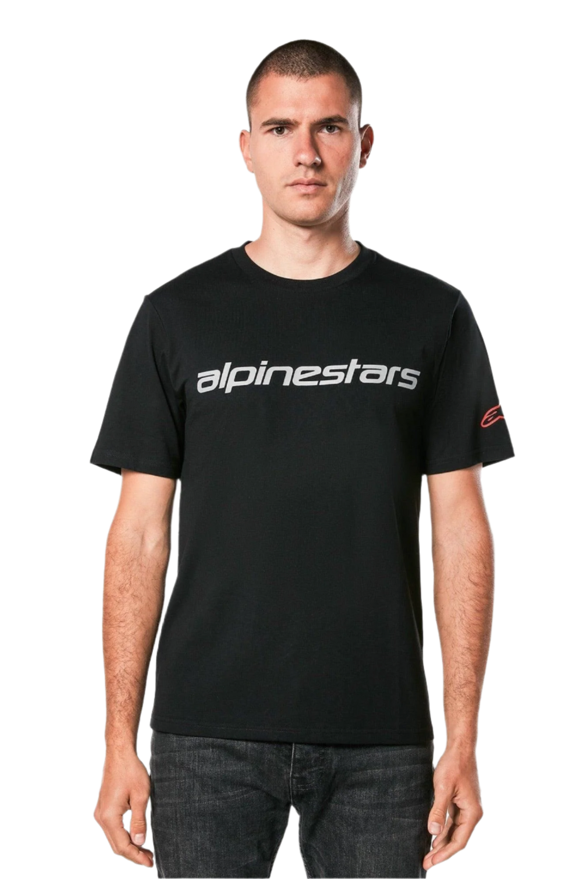 Alpinestars Linear Wordmark 2.0 CSF Tee, t-shirt de manga curta, preta, logótipo linear cinzento no peito e logótipo Ageless vermelho na manga, vestida por um modelo com jeans escuros, streetwear casual inspirado no desporto motorizado