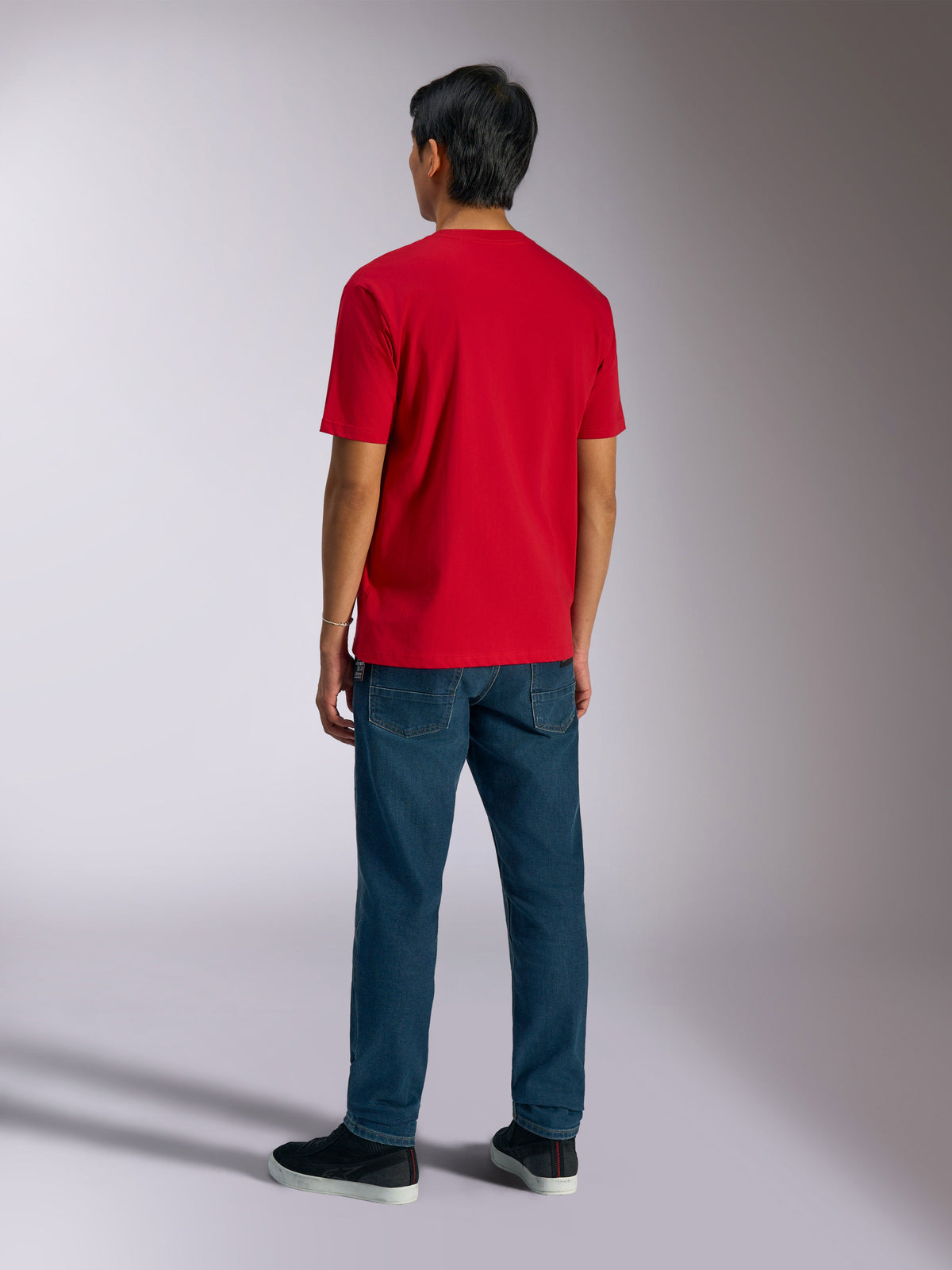 Alpinestars Ageless Shadow CSF Tee, t-shirt de manga curta, vermelha, vista traseira usada por modelo com calças de ganga azuis e sapatilhas pretas, casual motorsport streetwear