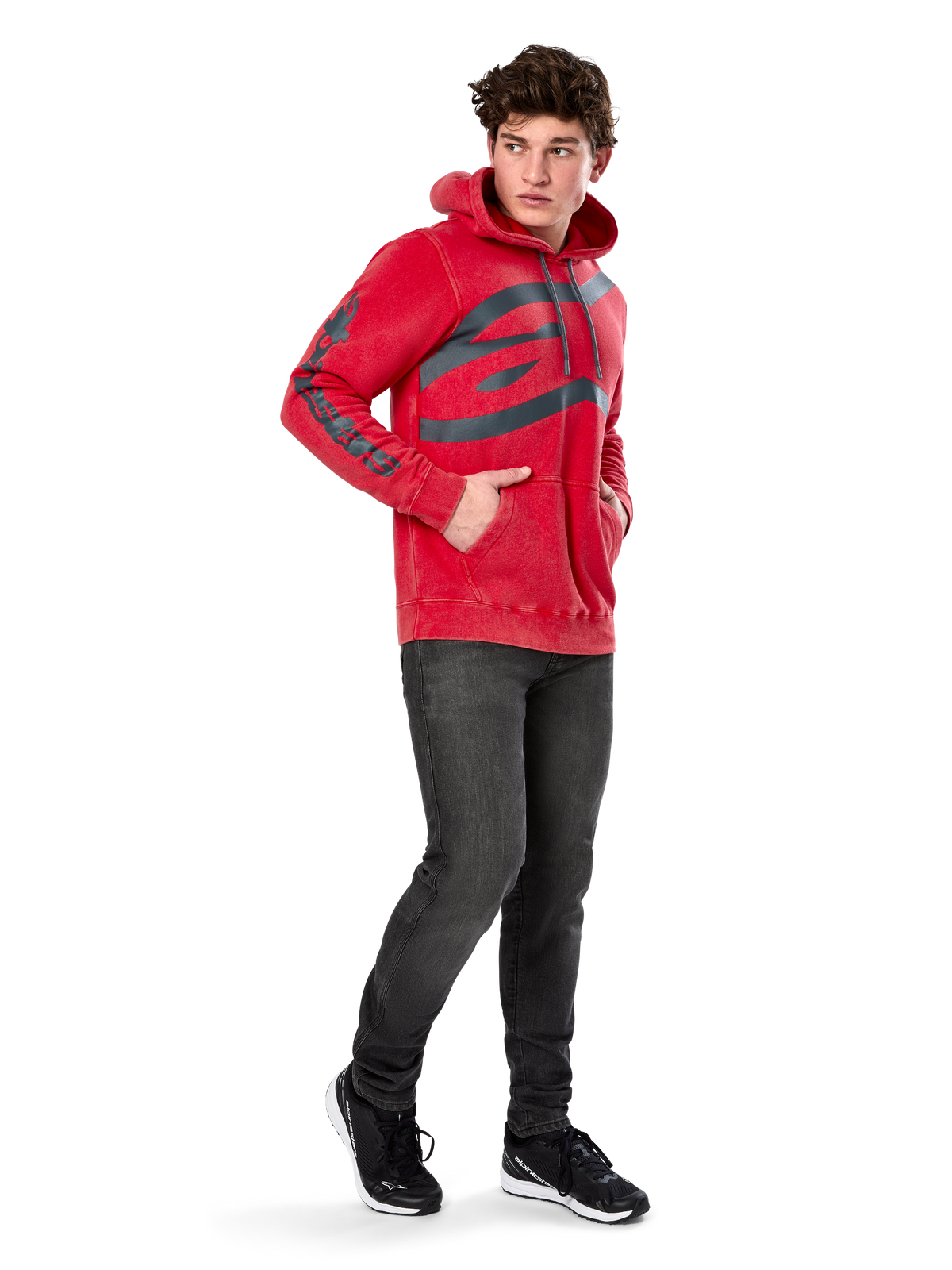 Alpinestars Unbound Hoodie, hoodie em malha tingida vermelha, logótipo escuro extragrande no peito e marca nas mangas, bolso canguru, capuz com cordão, usado por modelo com calças de ganga cinzento escuro e sapatilhas pretas, streetwear casual de inspiração motorizada