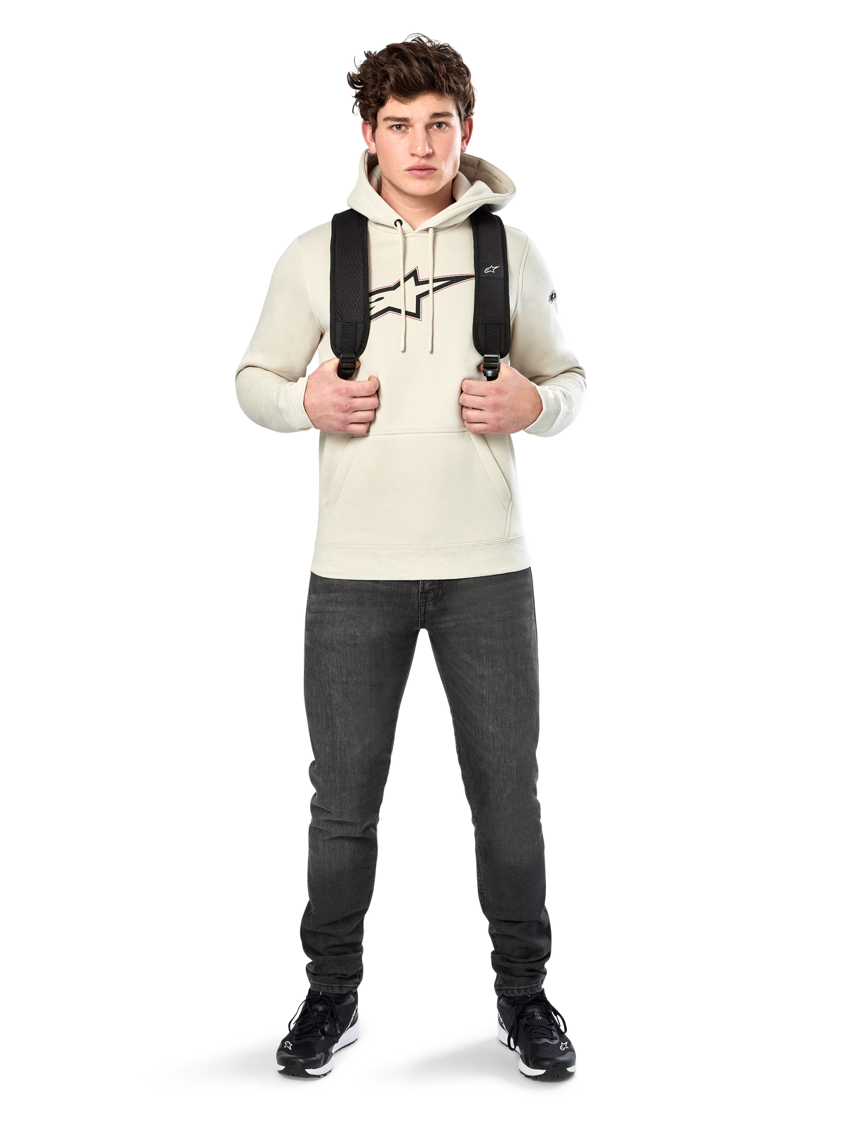 Alpinestars Insignia Hoodie, streetwear casual, hoodie Off White, logótipo com aspeto de fibra de carbono e contorno vermelho, capuz com cordão, bolso canguru, usado por modelo com mochila preta e calças de ganga cinzento escuro