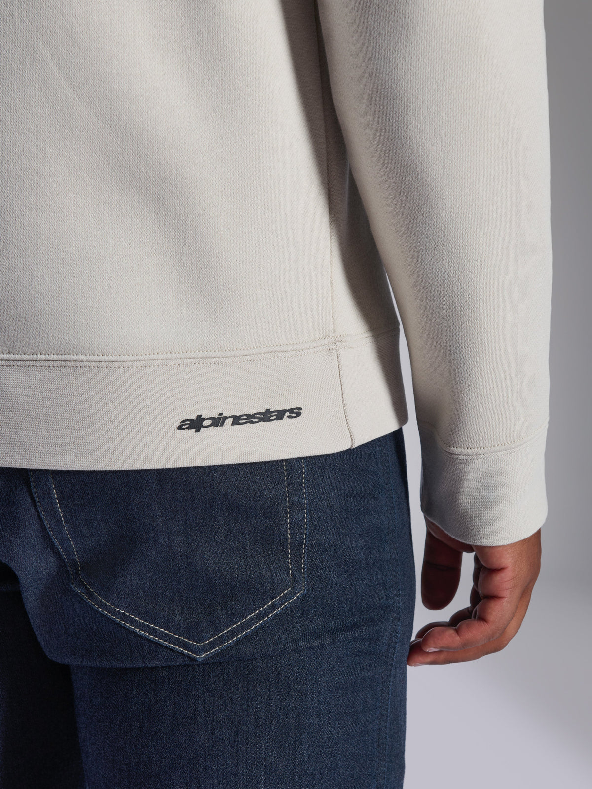 Sweatshirt Alpinestars Positive Crew, Off White, detalhe de grande plano da bainha e punho canelados, com pequeno logótipo Alpinestars a preto, vestuário casual inspirado no desporto motorizado