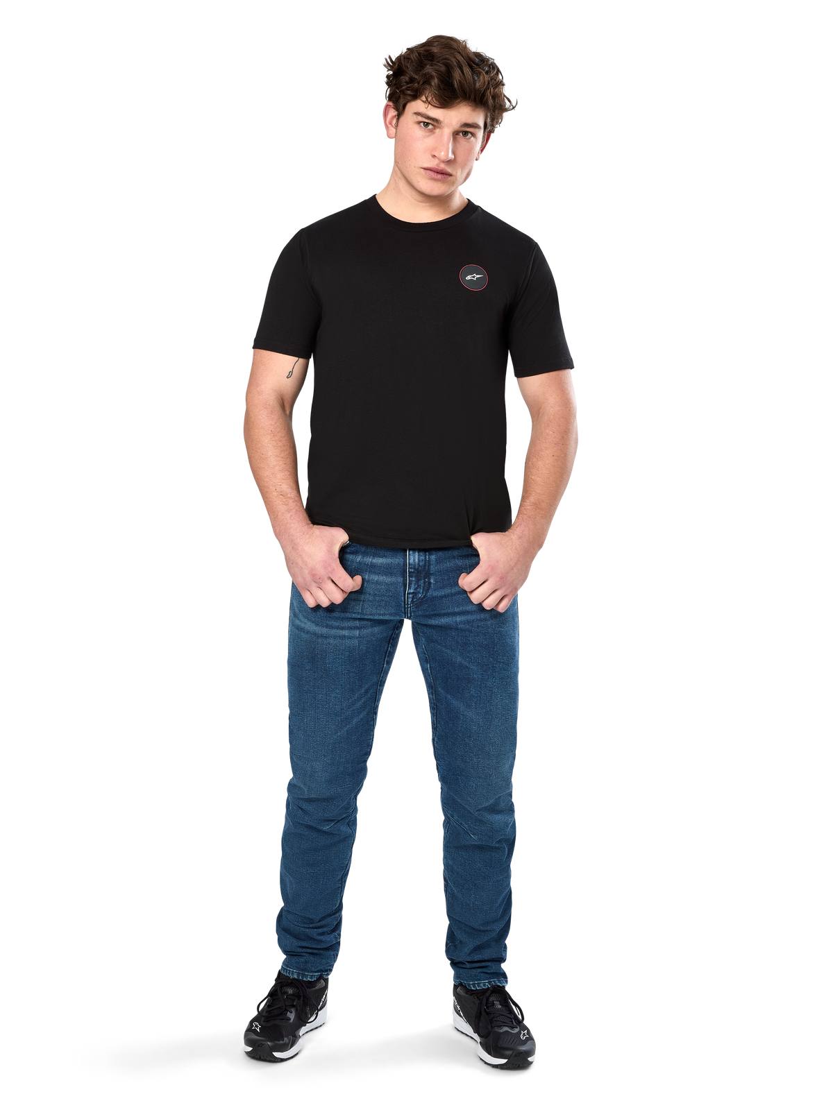 Alpinestars Dot Carbon CSF Tee, t-shirt de manga curta, preta, pequeno logótipo circular Astars Dot no peito, usada com calças de ganga azuis e ténis pretos, streetwear casual de motorsport