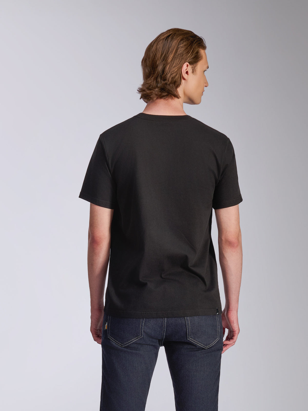 Alpinestars T-shirt Luxo CSF, t-shirt de manga curta, preta, vista traseira, vestida por um modelo com calças de ganga azul-escuro, streetwear casual inspirado no desporto motorizado