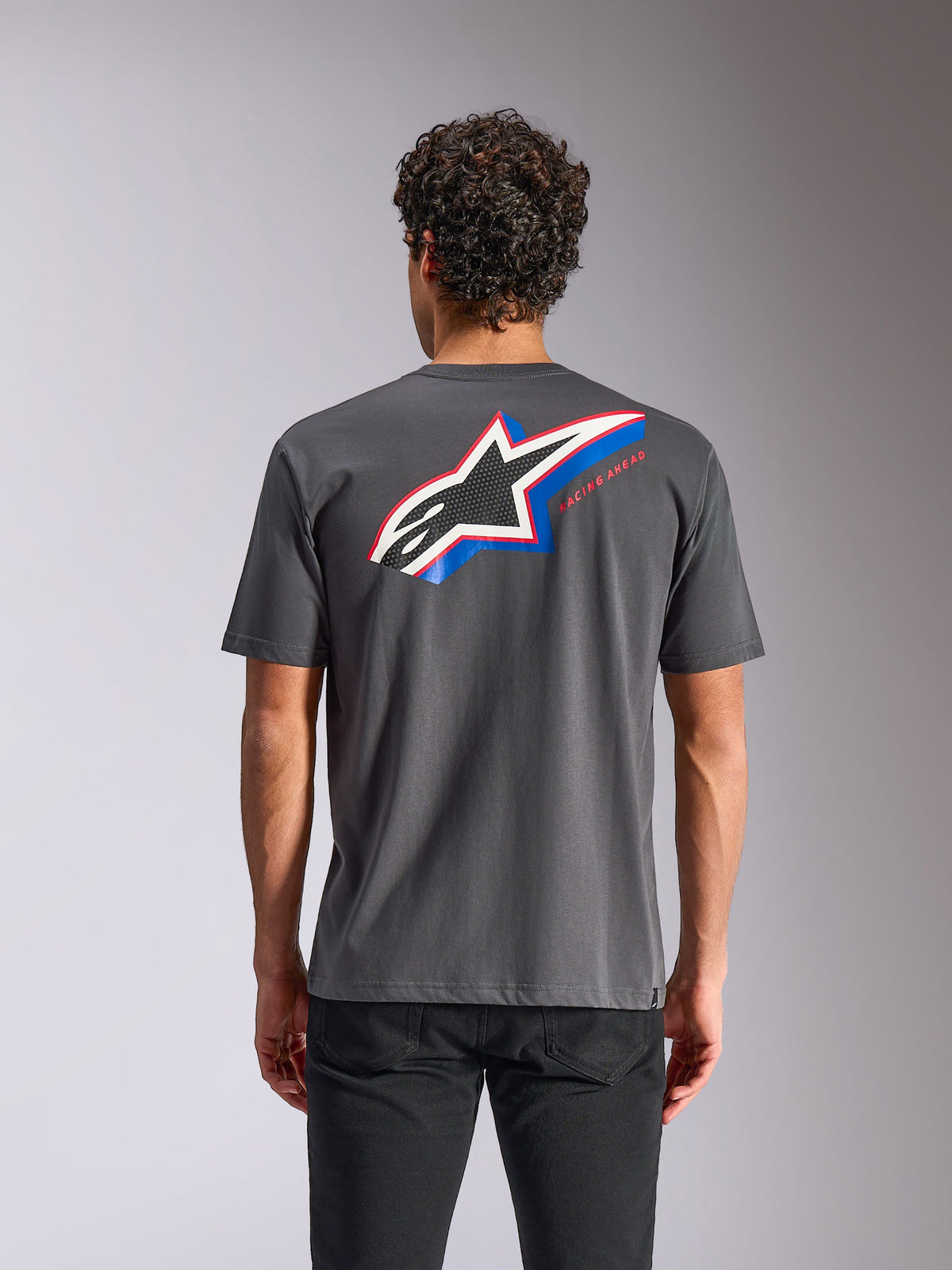 Alpinestars Angler CSF Tee, t-shirt de manga curta, cinzento carvão, vista traseira com um grande logótipo Astars com detalhes em azul e vermelho e o texto 'RACING AHEAD', streetwear casual de motorsport
