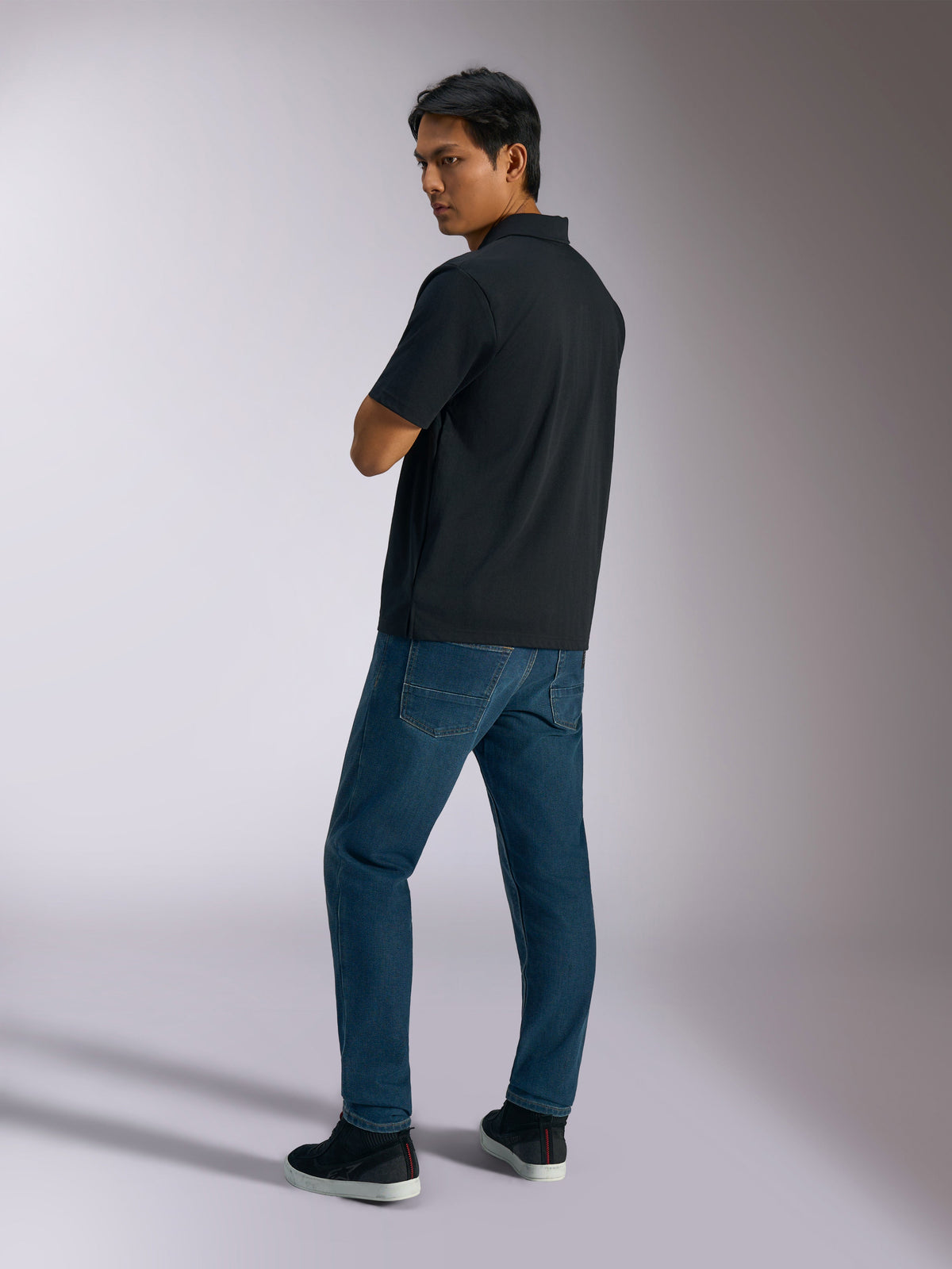 Polo Alpinestars Impetus Sport, preto, polo de manga curta com textura de malha simulada e carcela de três botões, usado por um modelo com calças de ganga azuis e ténis pretos, streetwear casual inspirado no desporto motorizado