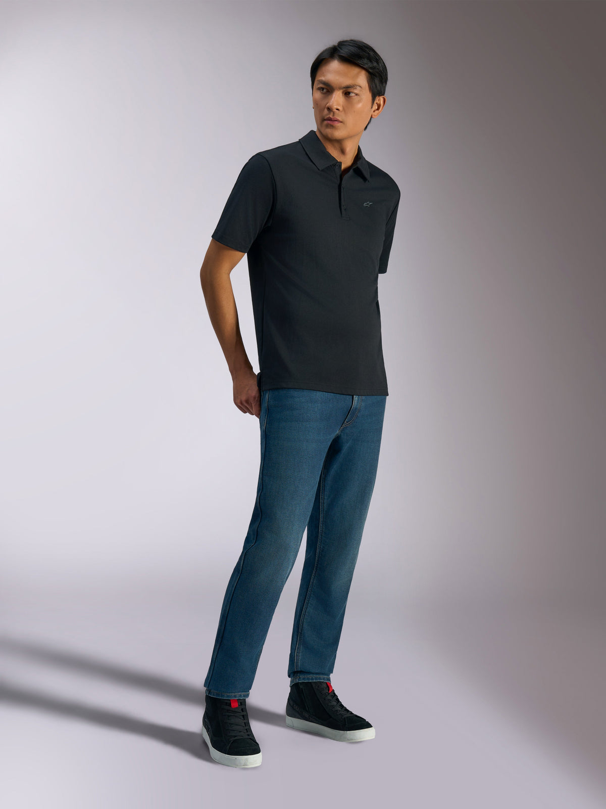 Alpinestars Polo Impetus Sport, polo de manga curta, preto, com um logótipo discreto no peito e carcela de três botões, usado por um modelo com calças de ganga azuis e sapatilhas pretas, vestuário casual de lifestyle inspirado no desporto motorizado