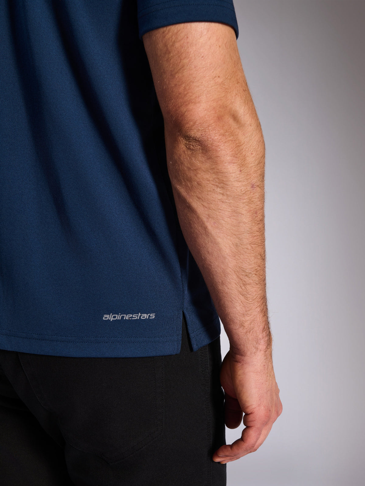 Alpinestars Impetus Sport Polo, Navy, Close-up of the lower hem showing the Alpinestars wordmark and side vent, mock-mesh knit texture, casual motorsport sportswear
