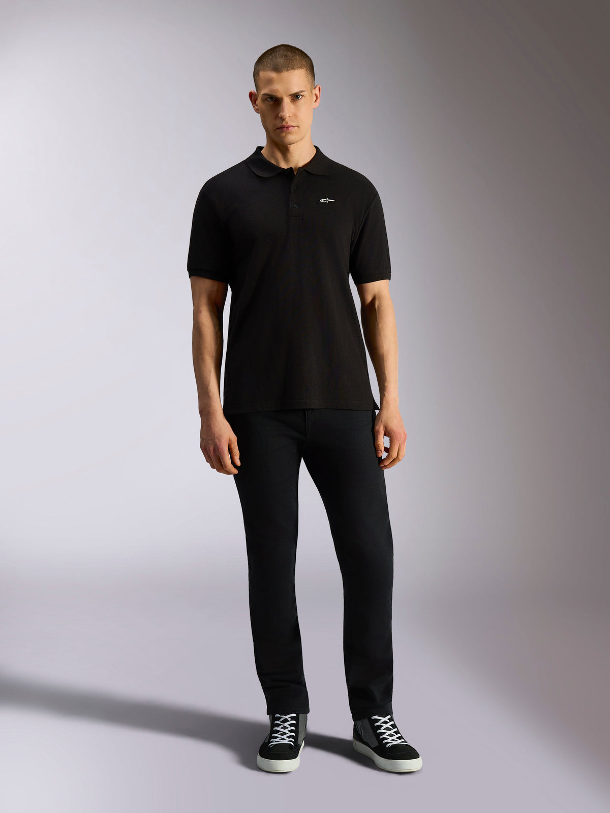 Polo Alpinestars Endeavor Classic, polo de manga curta em piqué, preto, pequeno logótipo Astars branco no peito, gola e punhos canelados, usado por modelo com calças pretas e sapatilhas, streetwear casual de desportos motorizados