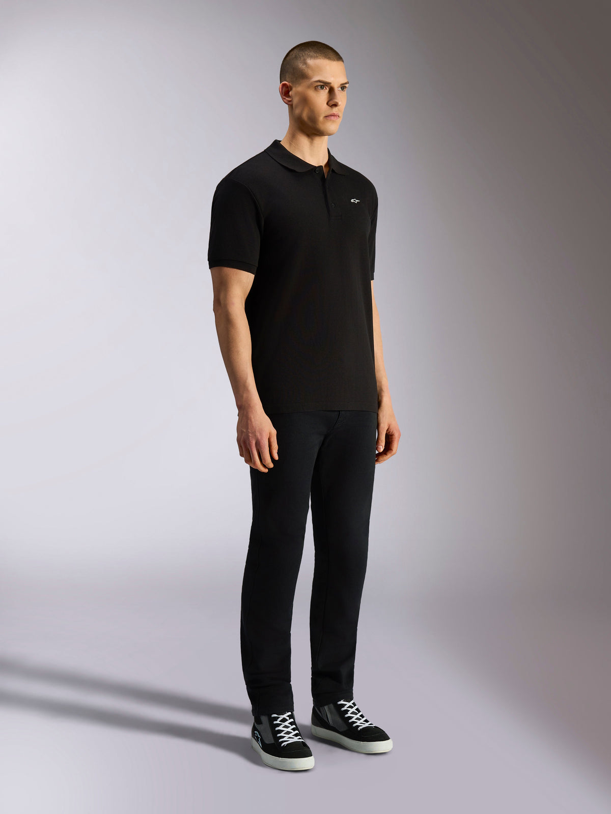 Polo Alpinestars Endeavor Classic, polo de manga curta preto em malha piqué com carcela de três botões, pequeno logótipo Astars branco no lado esquerdo do peito, usado com calças pretas e sapatilhas, streetwear casual de desportos motorizados