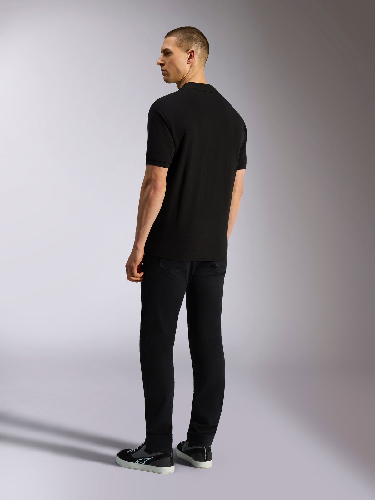 Alpinestars Endeavor Classic Polo, polo de manga curta em piqué, preto, vista traseira de modelo masculino a usar calças pretas e sapatilhas, streetwear casual inspirado no desporto motorizado