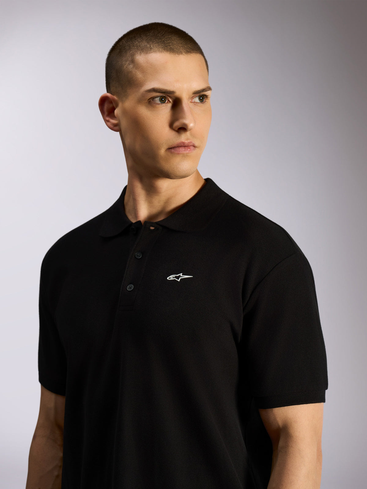 Polo Alpinestars Endeavor Classic, polo em piqué preto usado por um modelo masculino, pequeno logótipo Astars branco no peito, carcela de três botões e gola canelada, streetwear casual de desportos motorizados