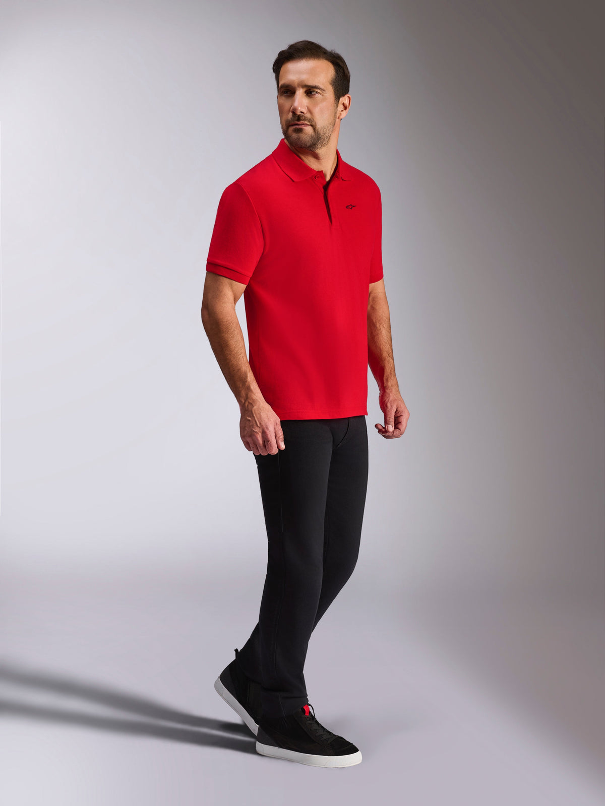 Alpinestars Endeavor Classic Polo, Red Short Sleeve Pique Polo, small black Astars logo, ribbed collar and cuffs, worn by a model with black pants and sneakers, casual motorsport-inspired streetwear
