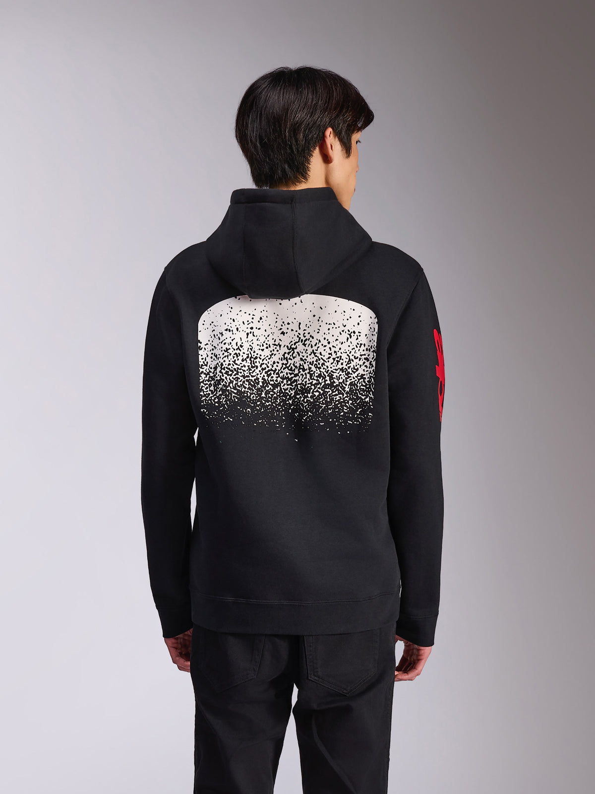 Alpinestars Obsessed Hoodie, vista traseira de camisola com capuz preta em fleece, com um grande gráfico de gradação MX salpicado a branco nas costas e logótipos Alpinestars vermelhos nas mangas, streetwear casual inspirado no desporto motorizado