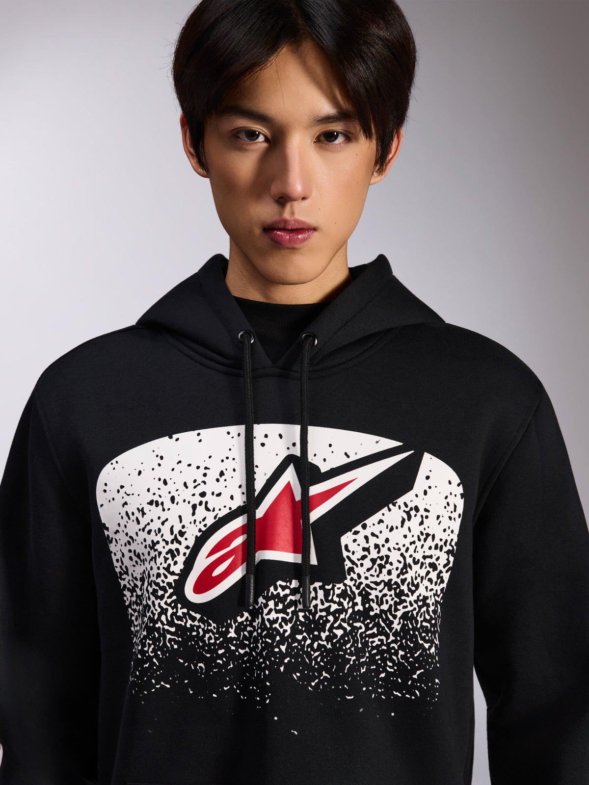 Alpinestars Obsessed Hoodie, hoodie em fleece preto, com logótipo Astars vermelho e branco dentro de um grafismo de gradação MX pontilhado a branco no peito, vestido por um modelo, streetwear casual de desportos motorizados com capuz de cordão ajustável