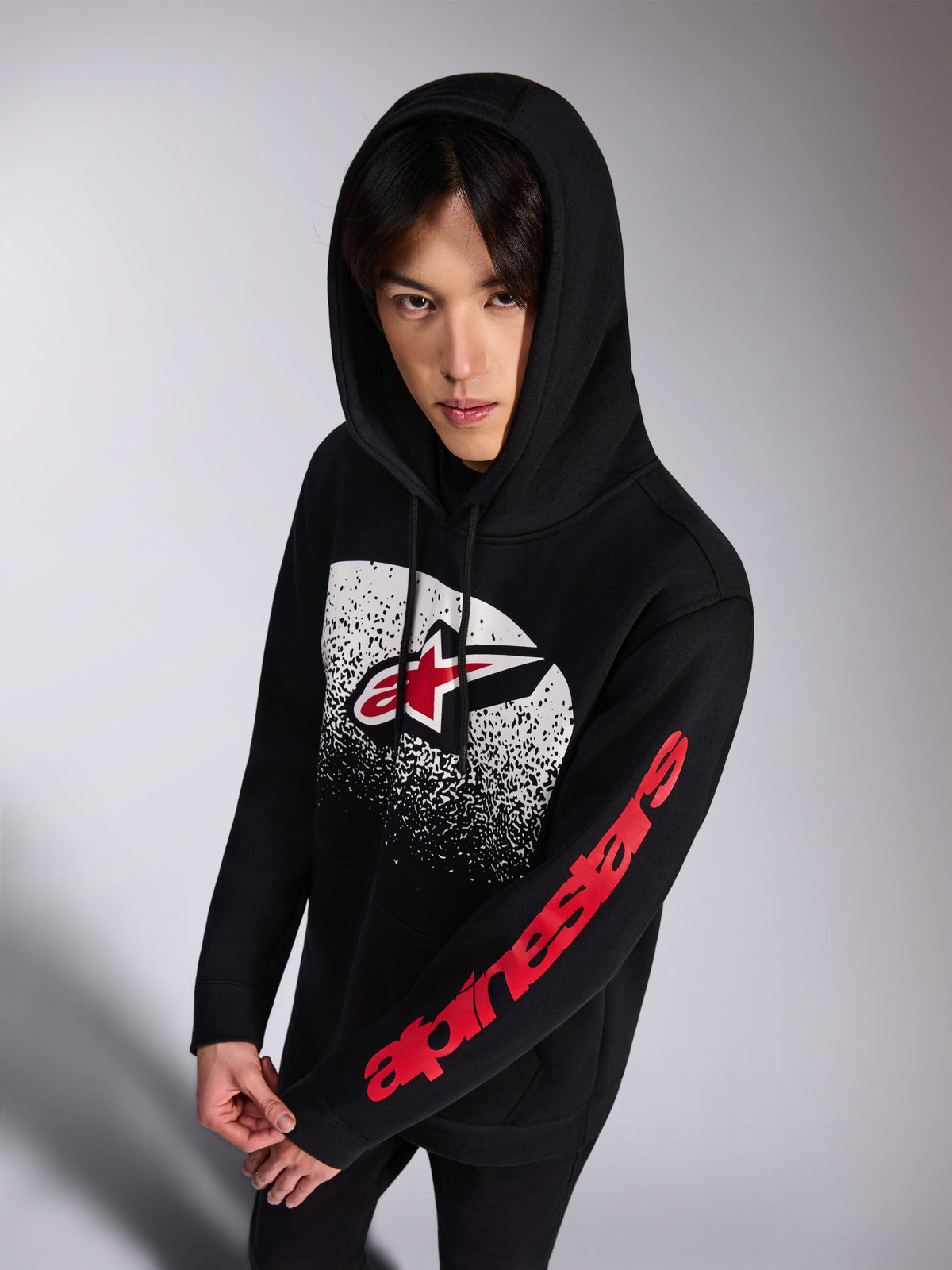 Alpinestars Obsessed Hoodie, camisola com capuz em fleece preta, logótipo Astars frontal vermelho e branco com gradação MX branca de efeito desgastado, logótipo Alpinestars vermelho na manga, capuz com cordões, streetwear casual inspirado no desporto motorizado