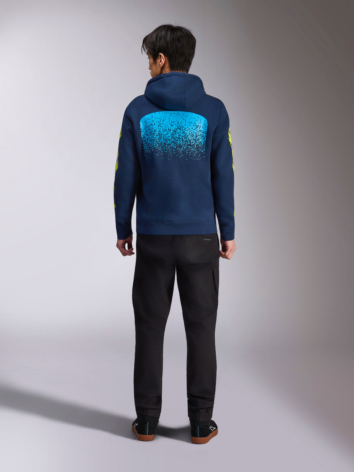 Alpinestars Obsessed Hoodie em azul-marinho, vista traseira com um grande gráfico de gradação MX em ciano e logótipos amarelos nas mangas, camisola de fleece casual inspirada no desporto motorizado