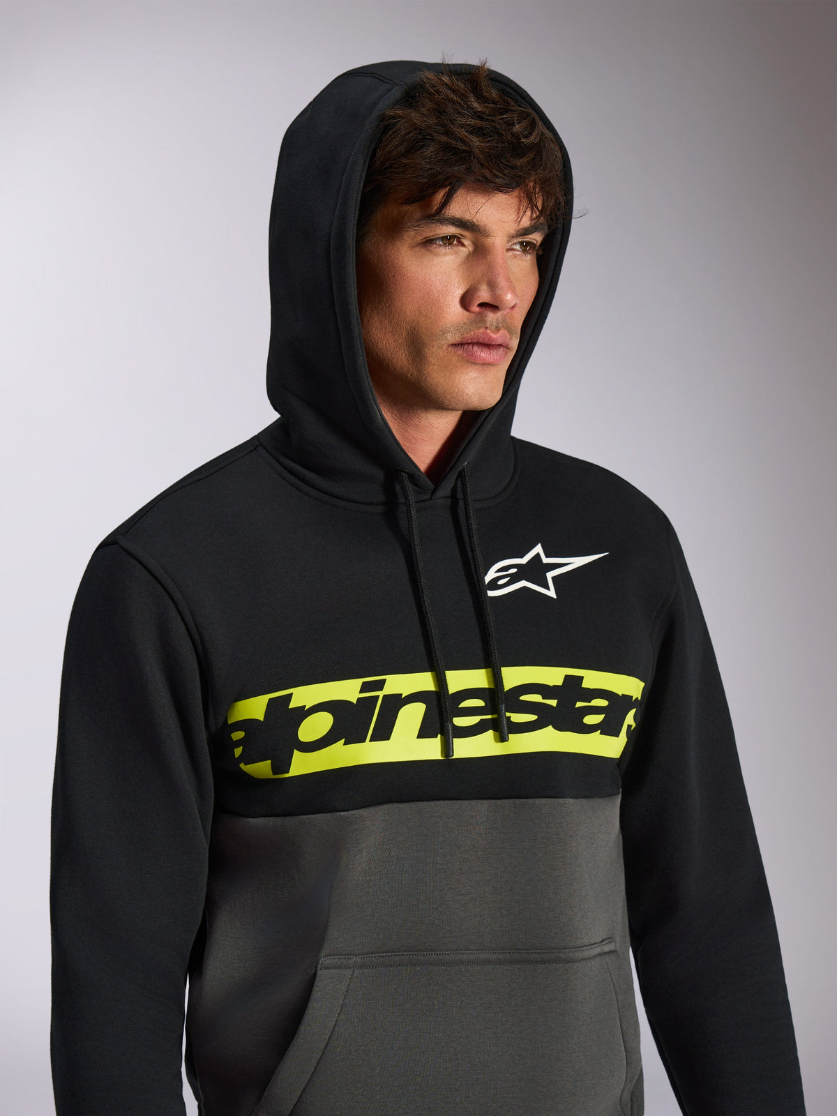 Alpinestars Parallel Hoodie, streetwear casual com blocos de cor, parte superior preta e parte inferior em cinzento gunmetal, faixa amarela néon no peito com logótipo Alpinestars em preto, logótipo Astars branco, camisola com capuz e cordão