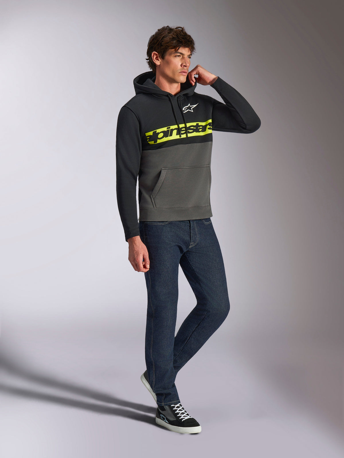 Alpinestars Parallel Hoodie, streetwear casual, com blocos de cor preto e cinzento gunmetal, logótipo Alpinestars em amarelo néon no peito, logótipo Astars branco, capuz com cordões, usado com calças de ganga escuras e sapatilhas