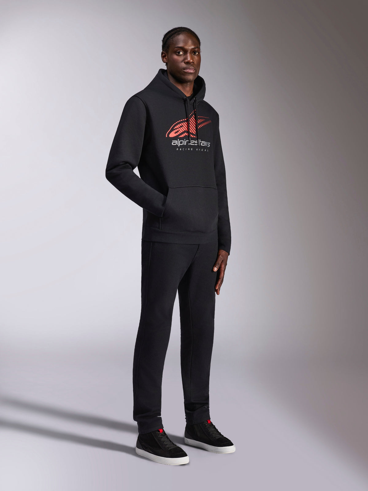 Alpinestars Pulse Hoodie, camisola com capuz preta, com logótipo Astars vermelho e branco com efeito speed line fade e texto Racing Ahead, usada com calças pretas a condizer e sapatilhas, streetwear casual inspirado no desporto motorizado