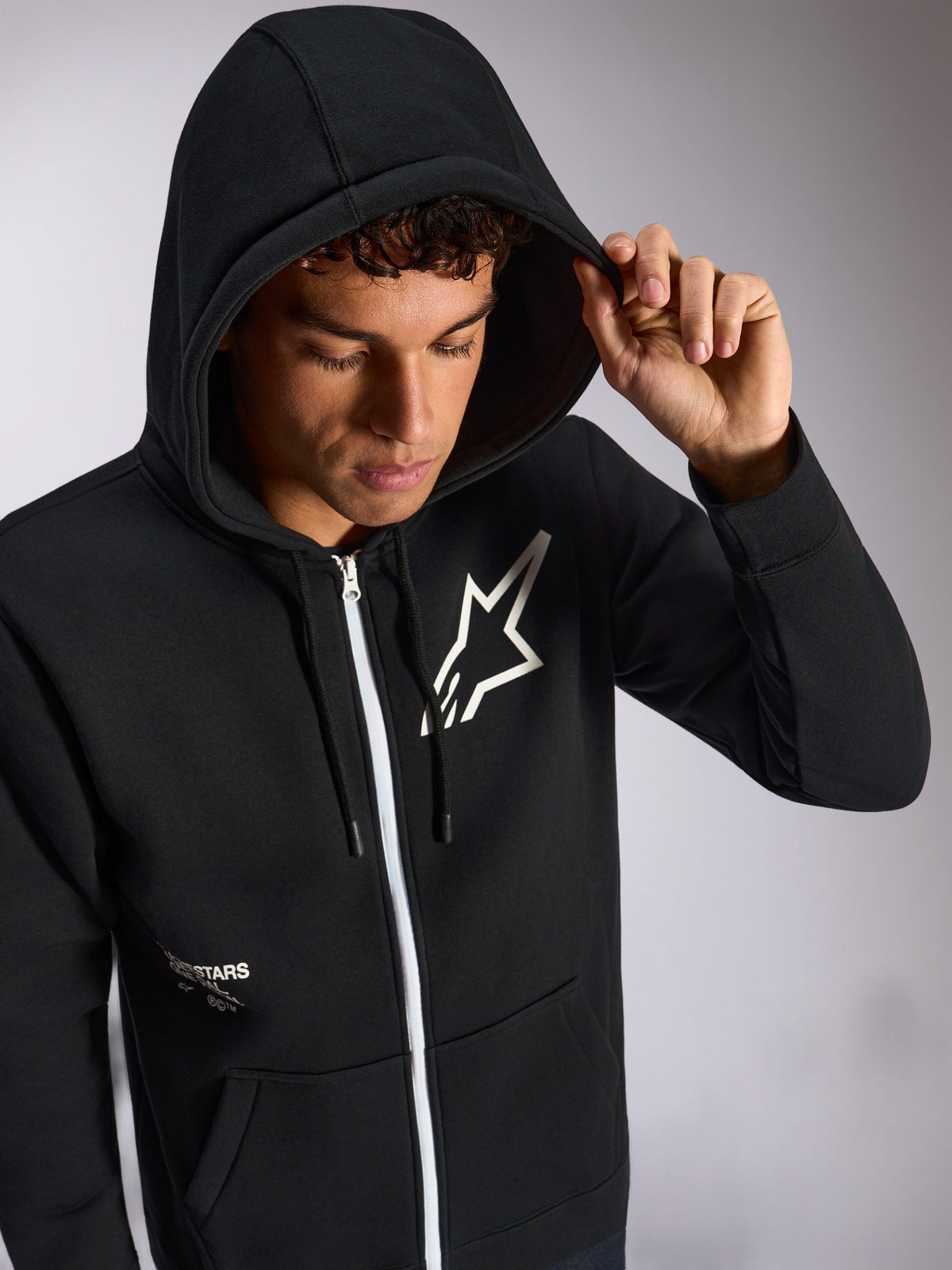 Alpinestars Transverse Hoodie, camisola preta com capuz e fecho frontal, logótipo Astars branco no peito, fecho de correr branco, capuz com cordão colocado, streetwear casual de inspiração motorsport