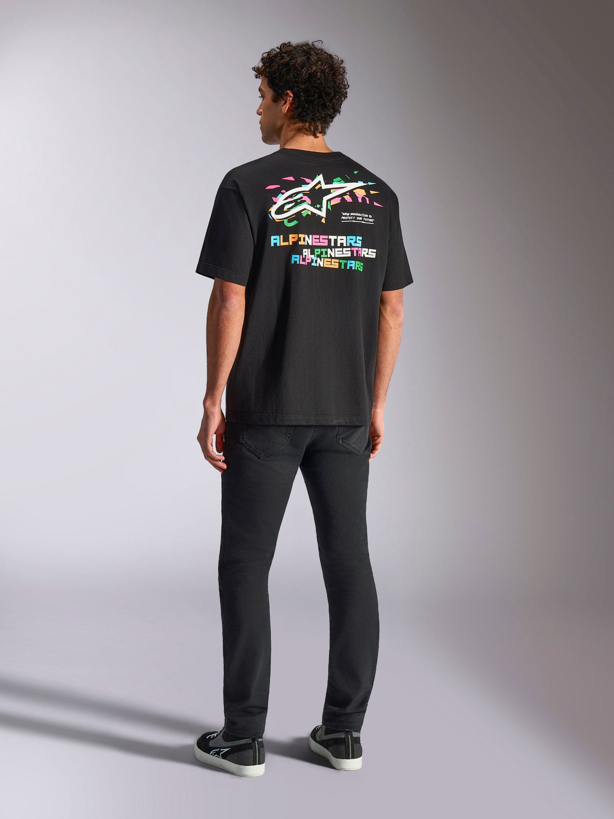 Alpinestars Wild Oversized CSF Tee, t-shirt de manga curta preta, com um grande gráfico multicolorido nas costas com o logótipo Astars e letras coloridas, corte oversized, combinada com calças pretas slim-fit para um visual casual streetwear