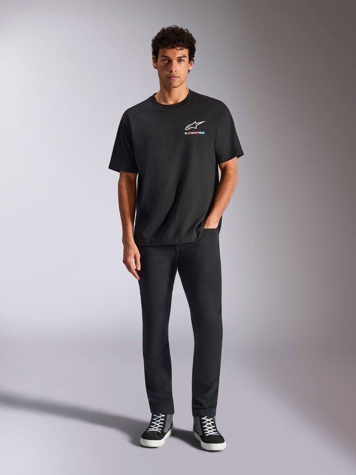 Alpinestars Wild Oversized CSF Tee, t-shirt de manga curta, preta, usada por um modelo com calças pretas e ténis, com um logótipo Astars branco e branding multicolorido vibrante, streetwear casual de desportos motorizados