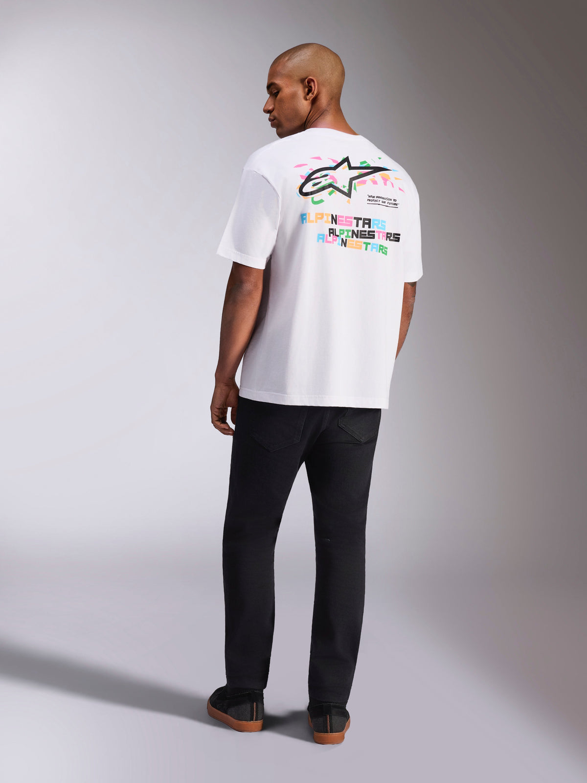 Alpinestars Wild Oversized CSF Tee, t-shirt de manga curta, branca, vista traseira de modelo a usar t-shirt oversized com logótipo Astars multicolor vibrante e texto empilhado nas costas, streetwear casual inspirado no desporto motorizado