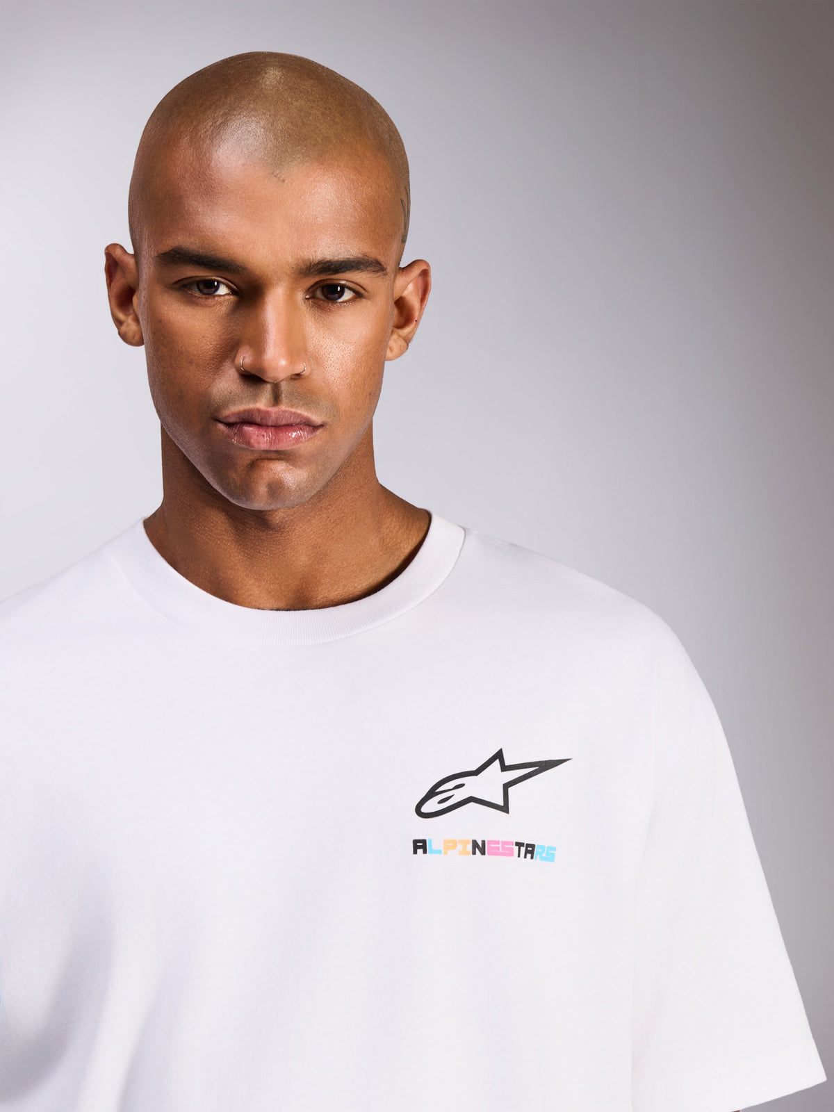 Modelo masculino a usar T-shirt Alpinestars Wild Oversized CSF, de manga curta, branca, com logótipo Astars preto e letras multicoloridas vibrantes no peito, estilo casual streetwear