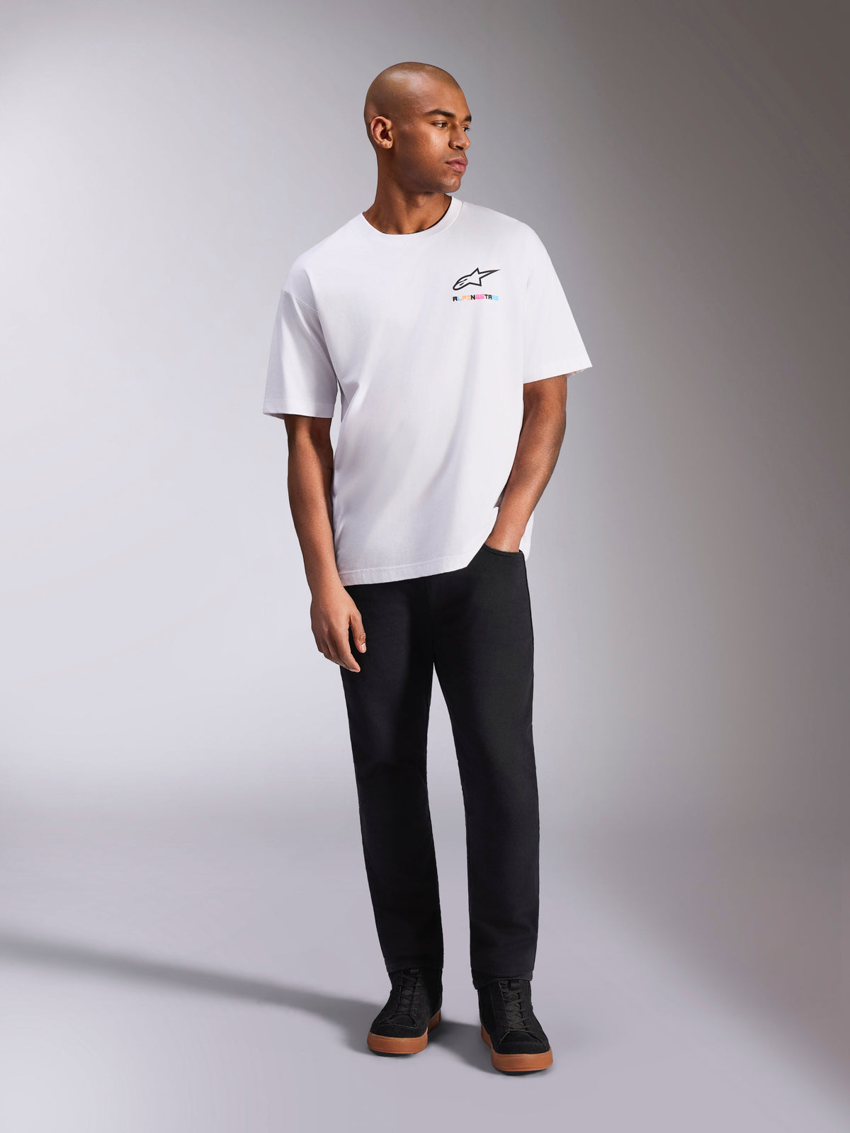 Alpinestars Wild Oversized CSF Tee, t-shirt de manga curta, branca, logótipo Astars multicolor vibrante no peito, usada com calças pretas e sapatilhas, vestuário casual de estilo de vida motorsport