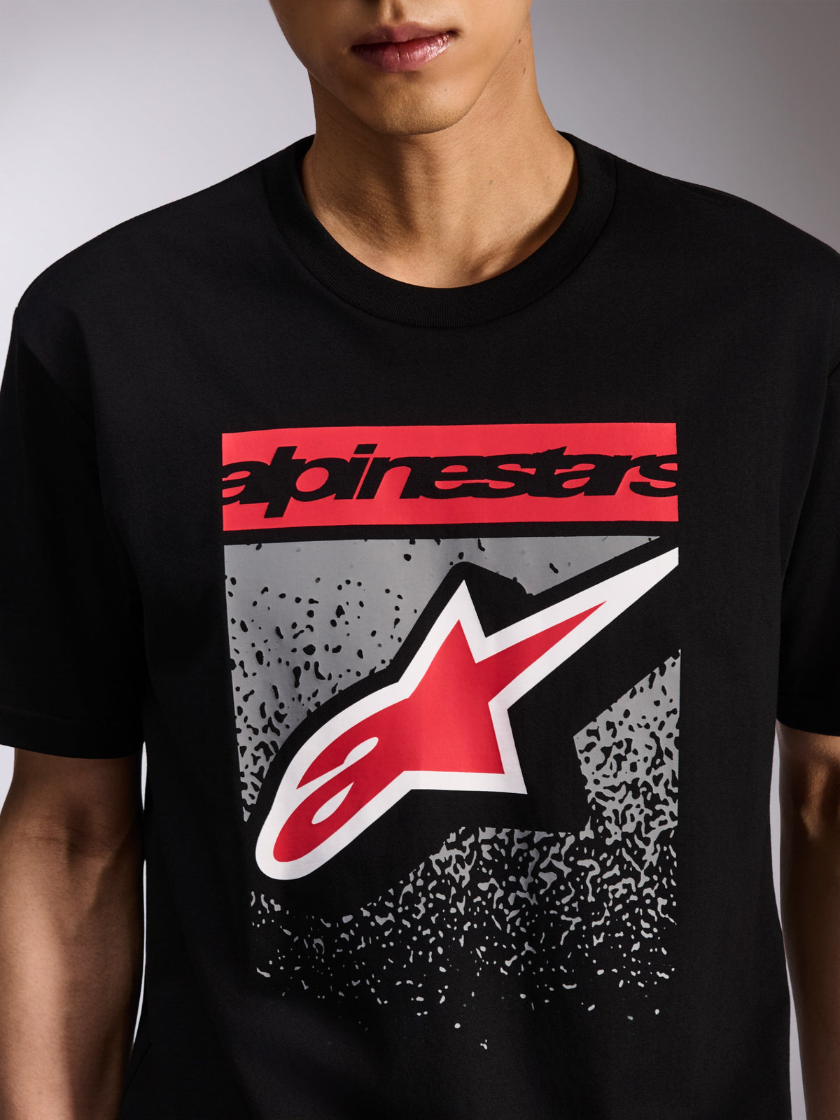 Alpinestars Noka CSF Tee, t-shirt de manga curta preta, grafismo frontal com lettering Alpinestars a vermelho e logótipo Astars em vermelho e branco sobre gradação MX cinzenta, estilo casual de motorsport