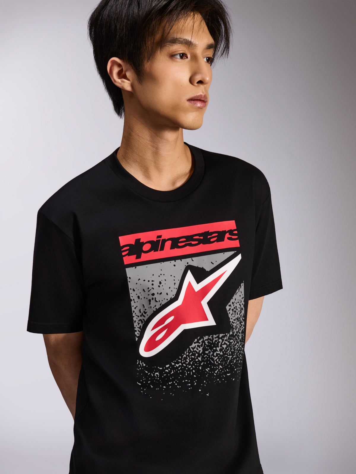 Alpinestars T-shirt Noka CSF, t-shirt de manga curta, preta, com um bloco de marca vermelho e logótipo Astars grande em vermelho e branco sobre um fundo cinzento texturado, streetwear casual de motorsport