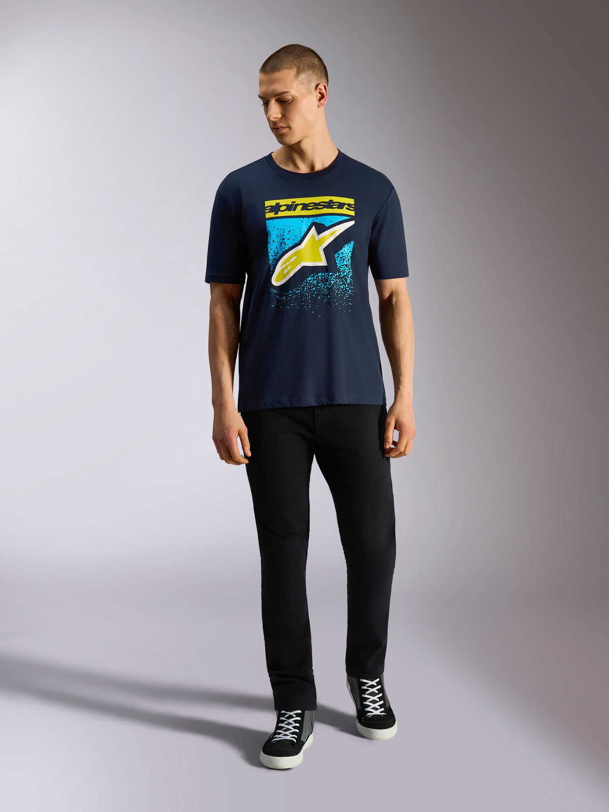 Alpinestars Noka CSF Tee, t-shirt de manga curta, azul marinho, logótipo Astars frontal com gradação MX amarela e azul claro, usada por um modelo com calças pretas, streetwear casual de inspiração motorsport