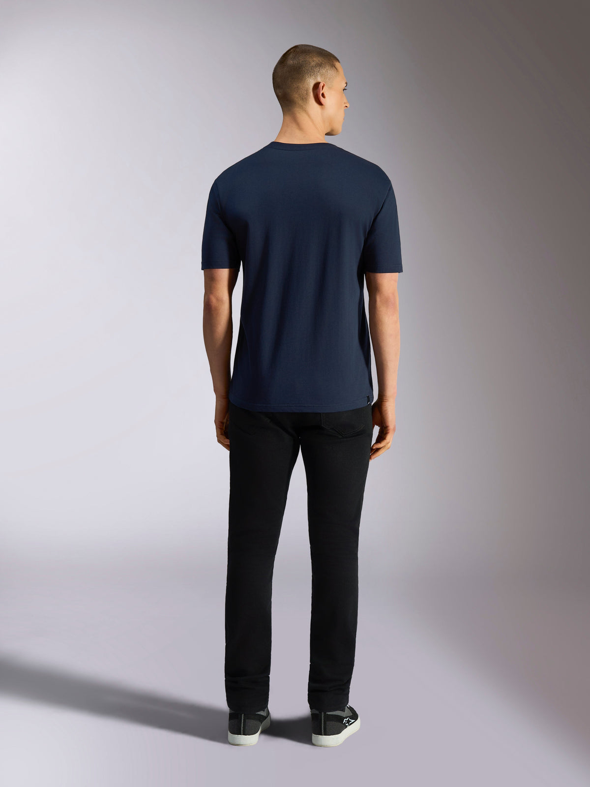 Alpinestars Noka CSF Tee, t-shirt de manga curta, azul marinho, vista traseira de um homem a usar a t-shirt combinada com calças pretas e sapatilhas, streetwear casual de motorsport