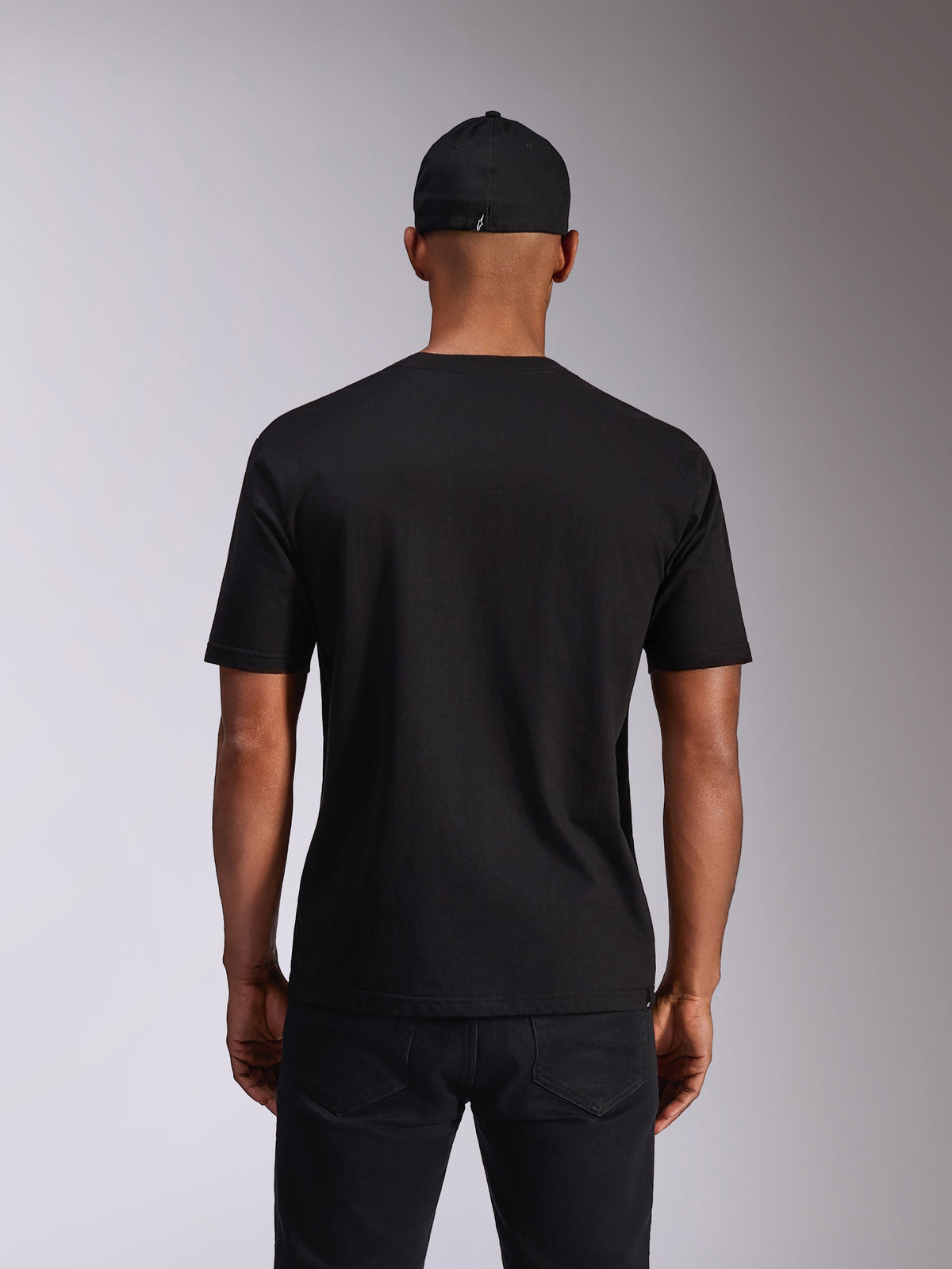Alpinestars Ellipsoid CSF Tee, t-shirt de manga curta, preta, vista traseira no modelo, usada com um boné preto e calças escuras, streetwear casual inspirado no desporto motorizado