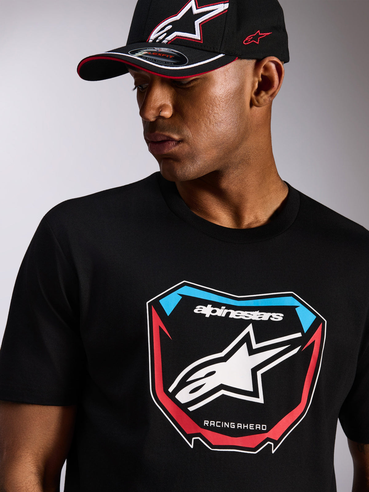 Alpinestars Plate CSF Tee, t-shirt de manga curta, preta, grande gráfico frontal MX Plate com logótipo de estrela e detalhes em vermelho e azul, usada com um boné Alpinestars preto a condizer, streetwear casual de desportos motorizados