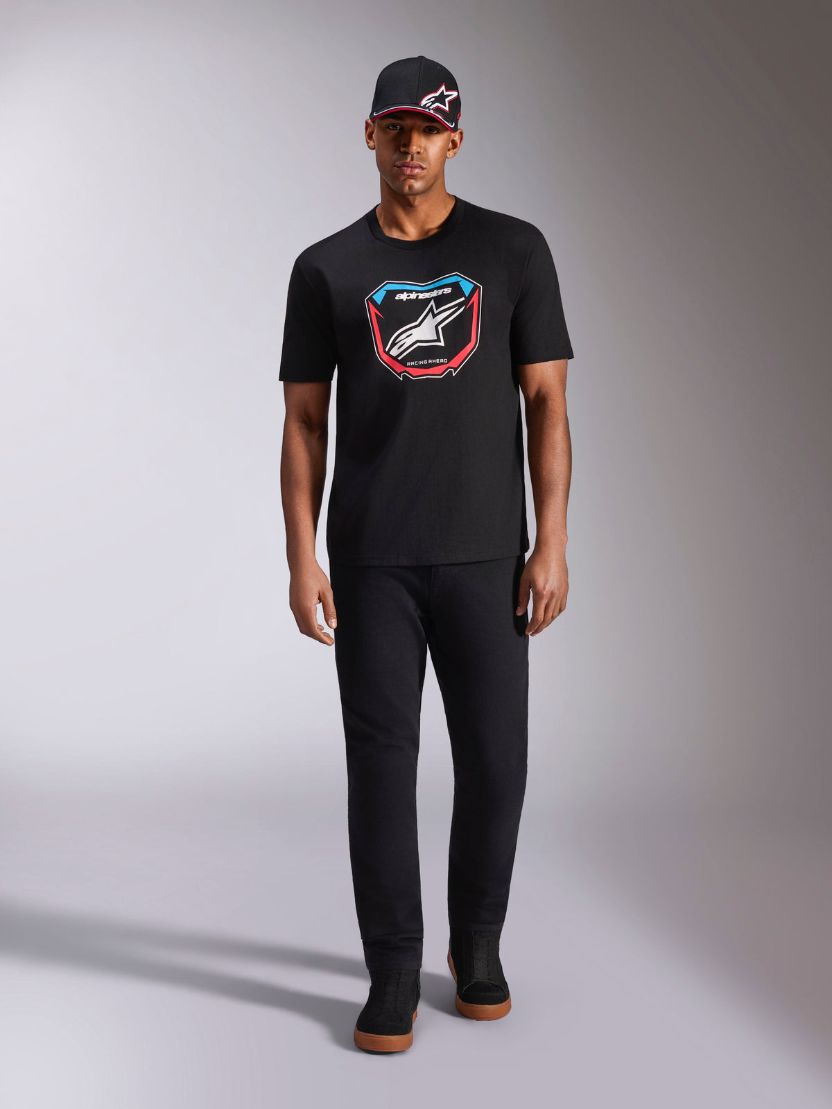 Alpinestars Plate CSF Tee, t-shirt de manga curta, preta, gráfico frontal MX plate com logótipo Astars branco e detalhes em azul e vermelho, vestida por modelo com boné e calças pretas a condizer, vestuário desportivo casual de motorsport