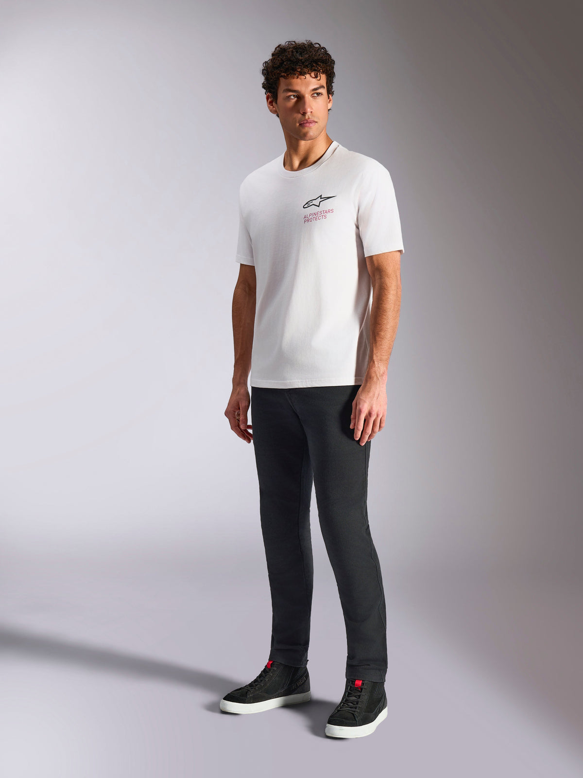 Alpinestars Pop Helmet CSF Tee, T-shirt de manga curta, branca, com logótipo Astars na frente e texto a vermelho, vestida por um modelo masculino com calças escuras e sapatilhas pretas, streetwear casual de motorsport