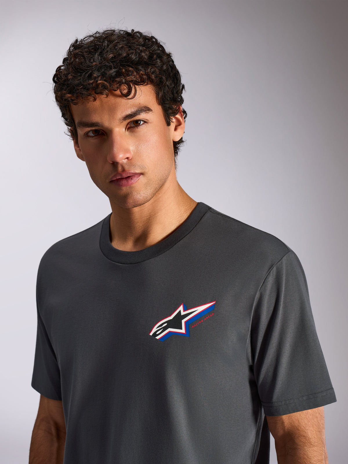 T-shirt Alpinestars Angler CSF, t-shirt de manga curta, cinzento carvão, vestida por um modelo masculino, com um logótipo Astars multicolor no peito, streetwear casual de desportos motorizados