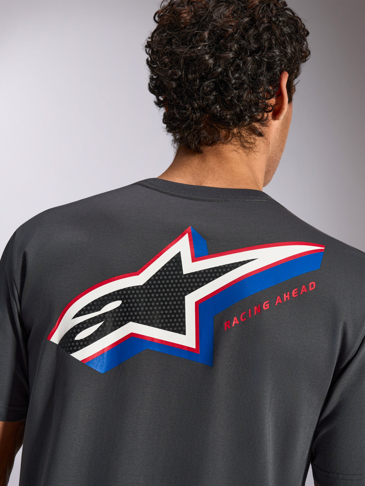Alpinestars Angler CSF Tee, t-shirt de manga curta, charcoal, vista traseira num modelo com grande logótipo de estrela da Alpinestars multicolor, preenchimento perfurado e texto "RACING AHEAD", streetwear casual de desportos motorizados